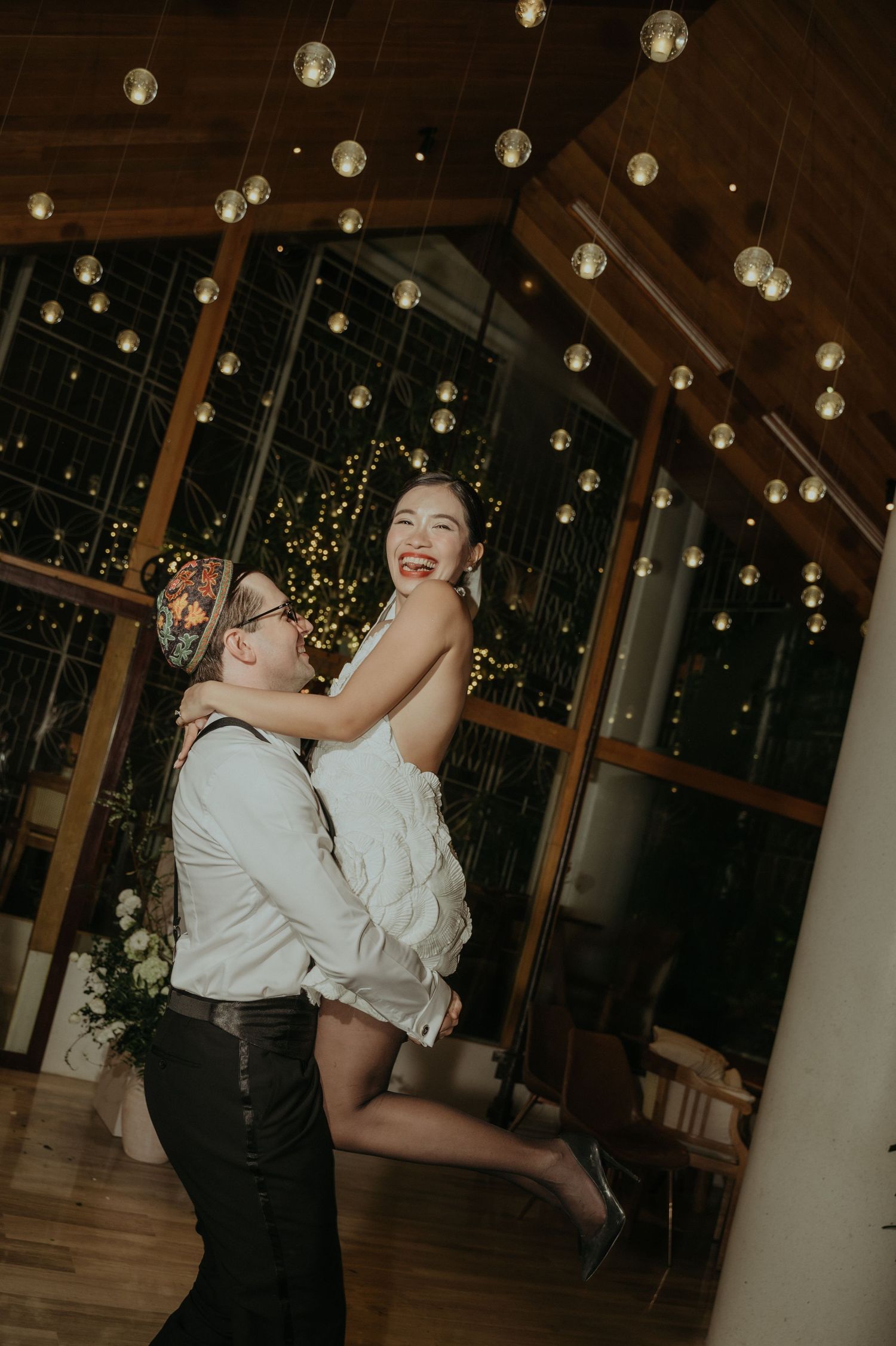 Couple sharing a joyful dance moment under suspended globe lights at their wedding reception.