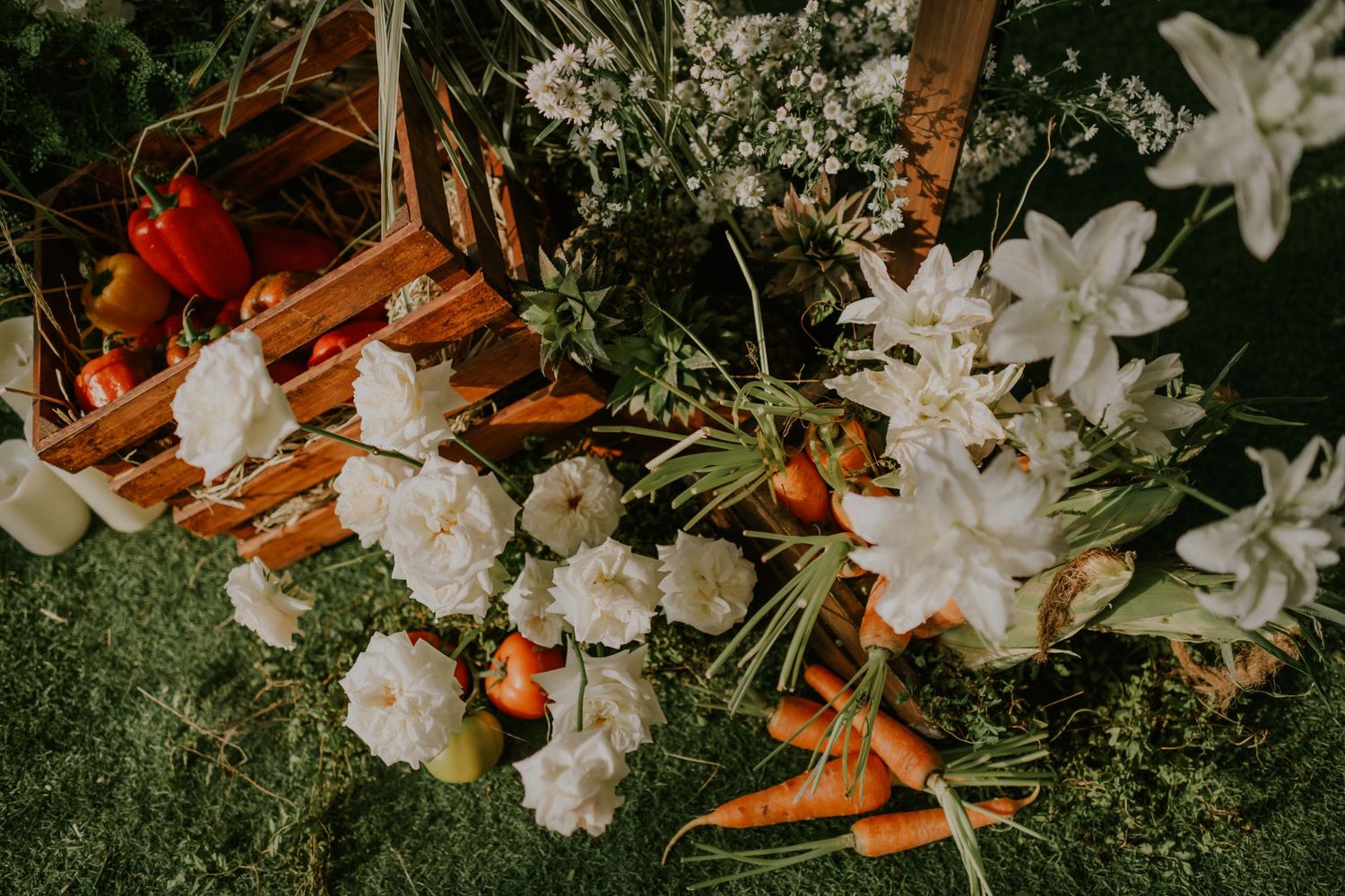 Artistic arrangement of white flowers, carrots, and botanicals on green surface.