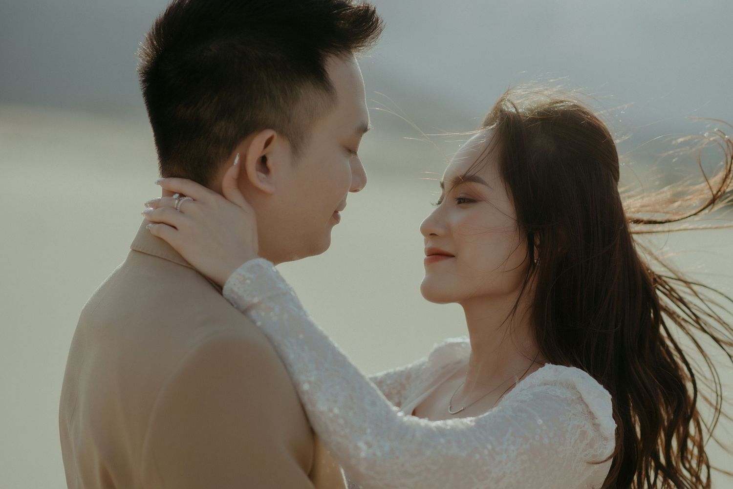 Romantic couple embracing during golden hour on a misty day with wind blowing through her dark hair.