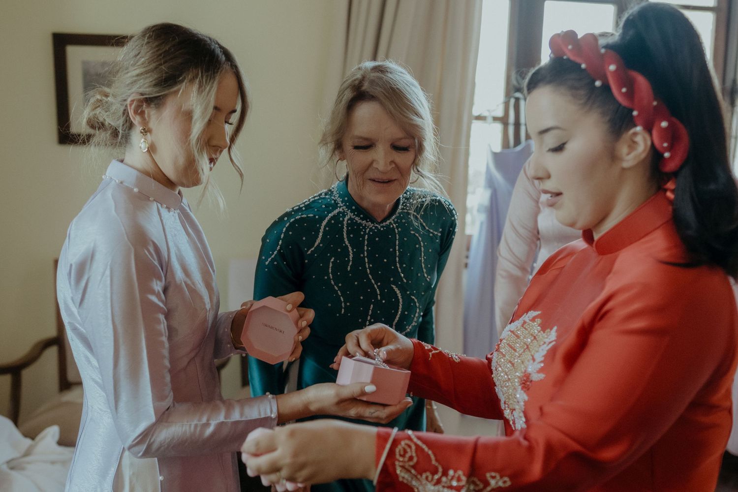 Three women in a casual indoor setting gather together looking at something small in their hands.