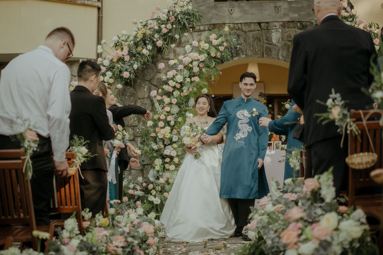 Wedding ceremony scene with elegant floral arch made of white roses and pink blooms decorating indoor venue.