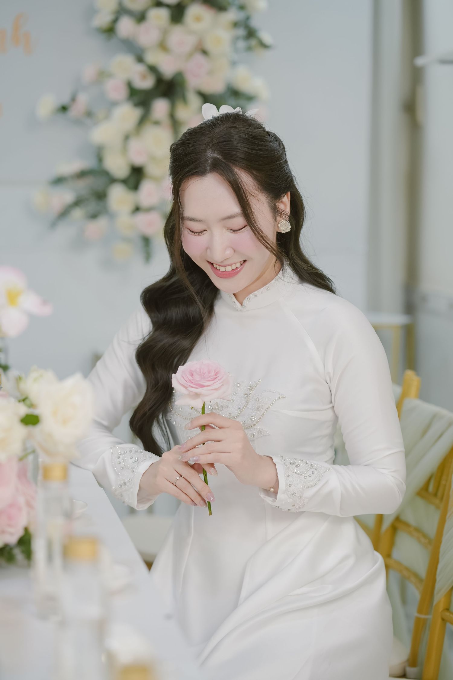 Delicate scene with white dress and pink rose against floral backdrop.