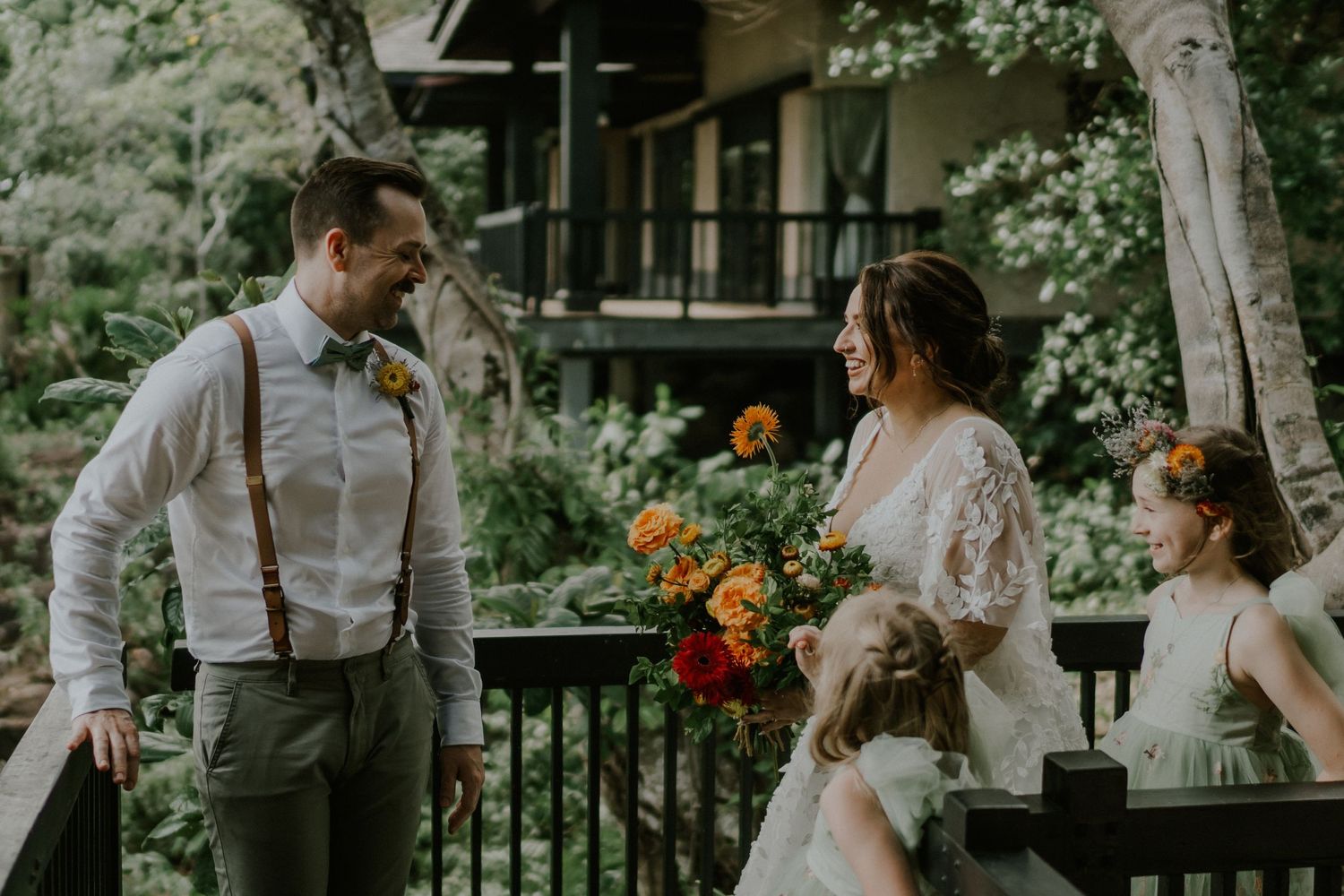 A joyful wedding scene with suspenders and lace details against a backdrop of tropical foliage.