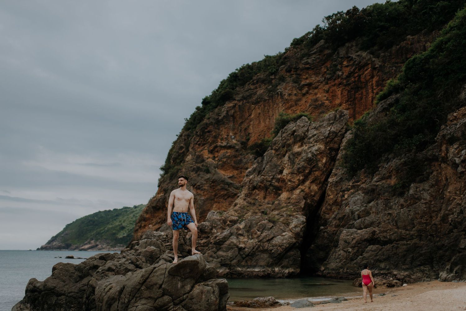 Adventure seekers climbing on coastal rock formations under cloudy skies.