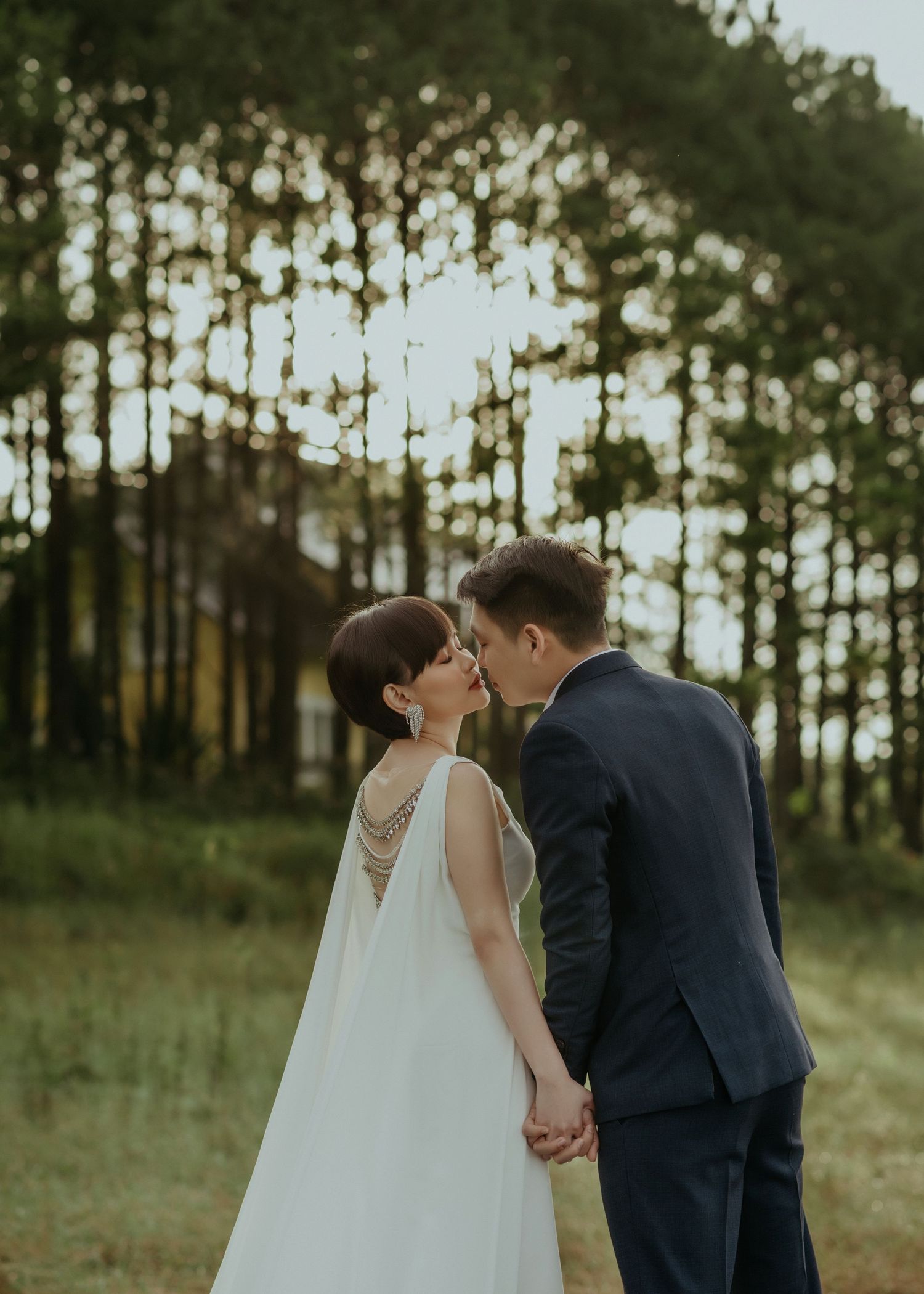 A tender moment captured between newlyweds in a sunlit forest, with the bride's elegant white gown flowing behind her.