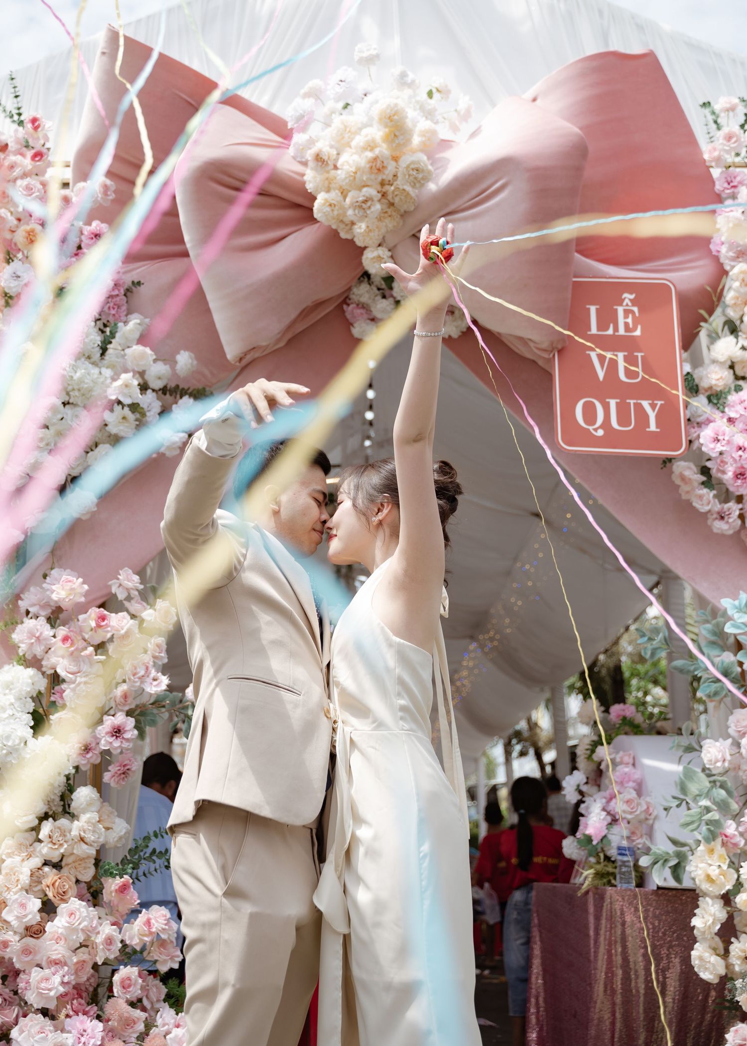 A couple stands beneath an elegant pink bow and floral arch with a white and blush color scheme.