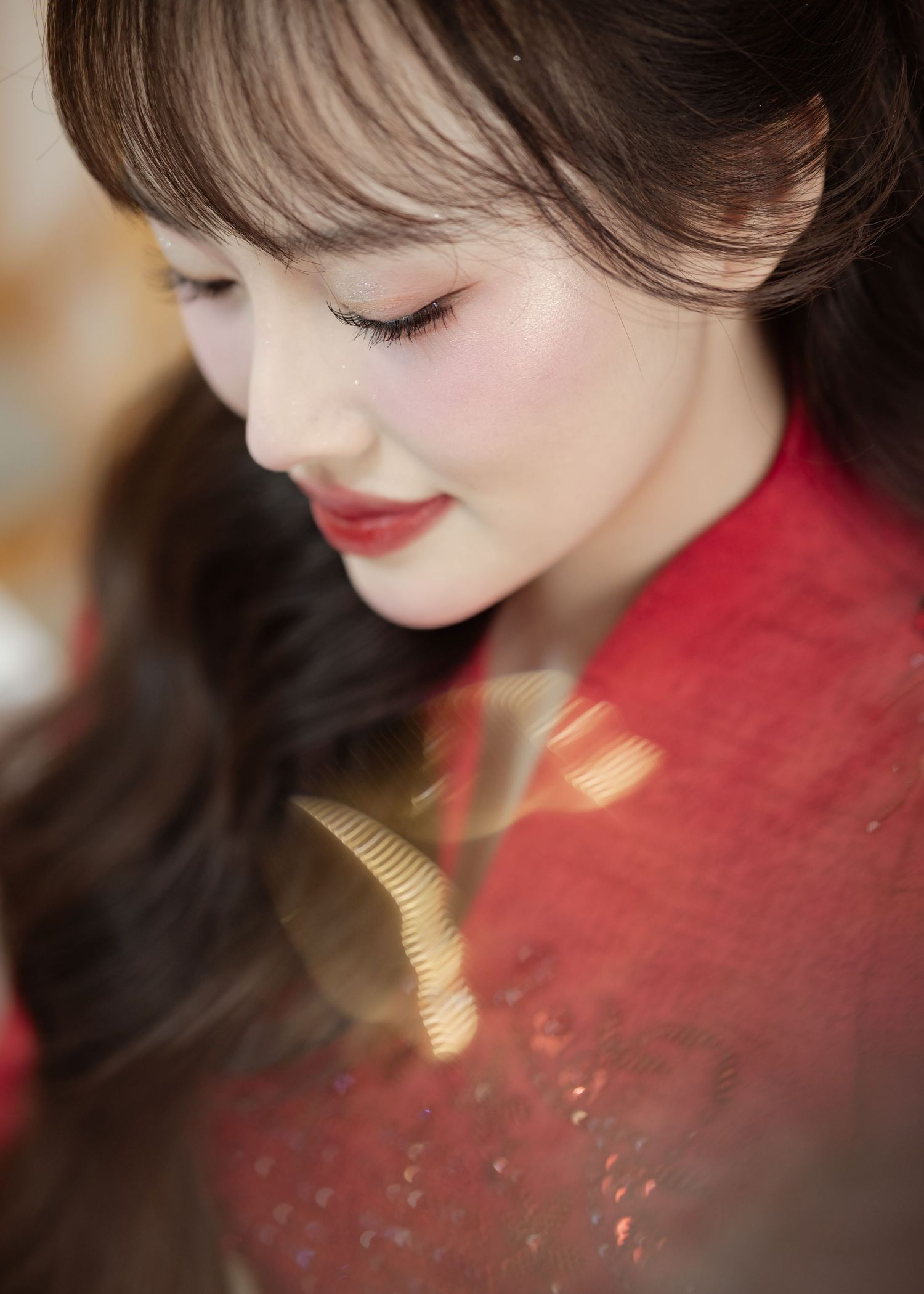 Side profile portrait of someone with brown hair wearing a traditional red dress with gold embellishments.