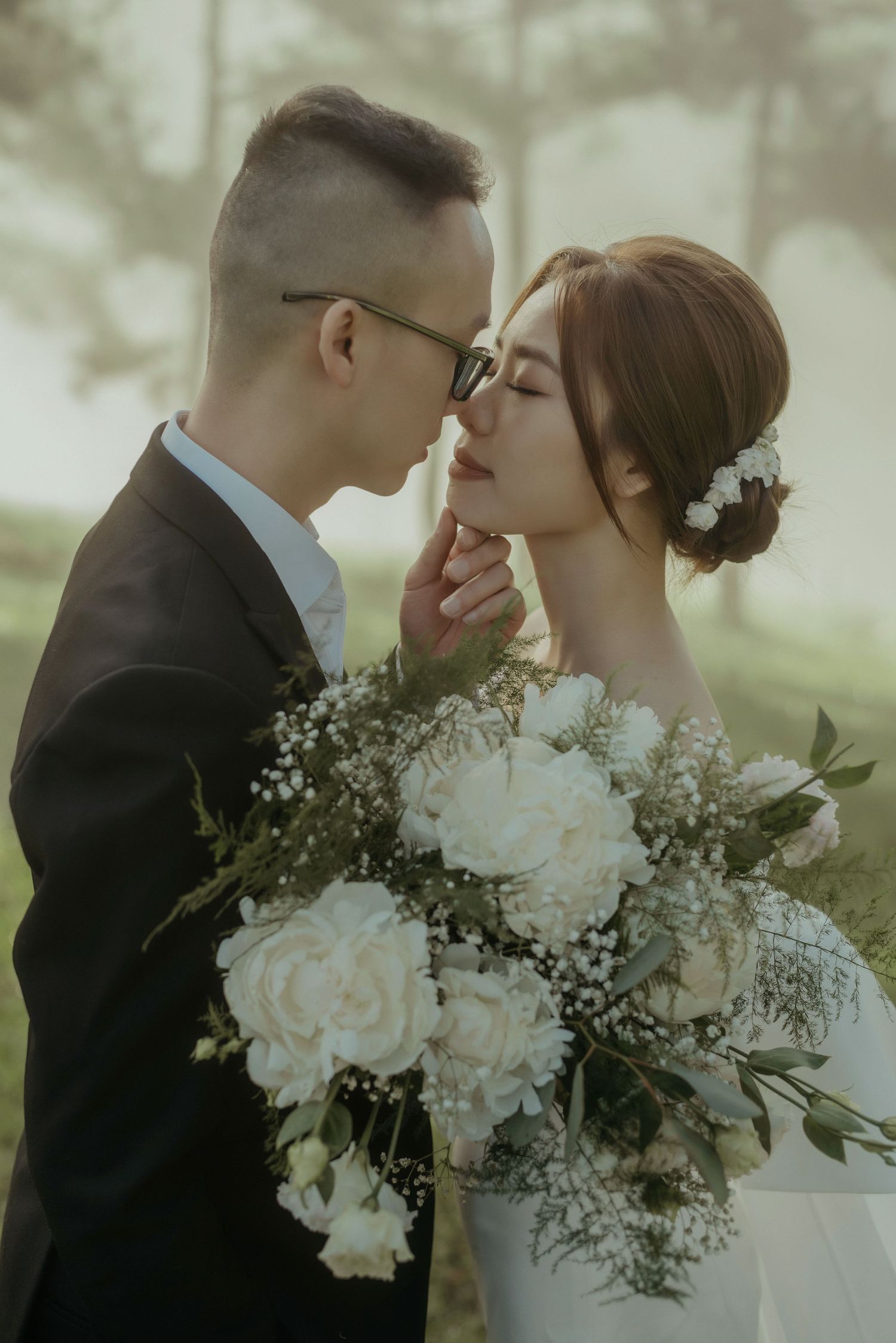 Intimate wedding moment captured at a misty outdoor venue with a beautiful white rose and baby's breath bouquet.