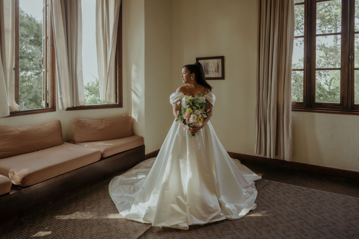 Beautiful ivory wedding gown with floral bouquet photographed in elegant room with natural window light.