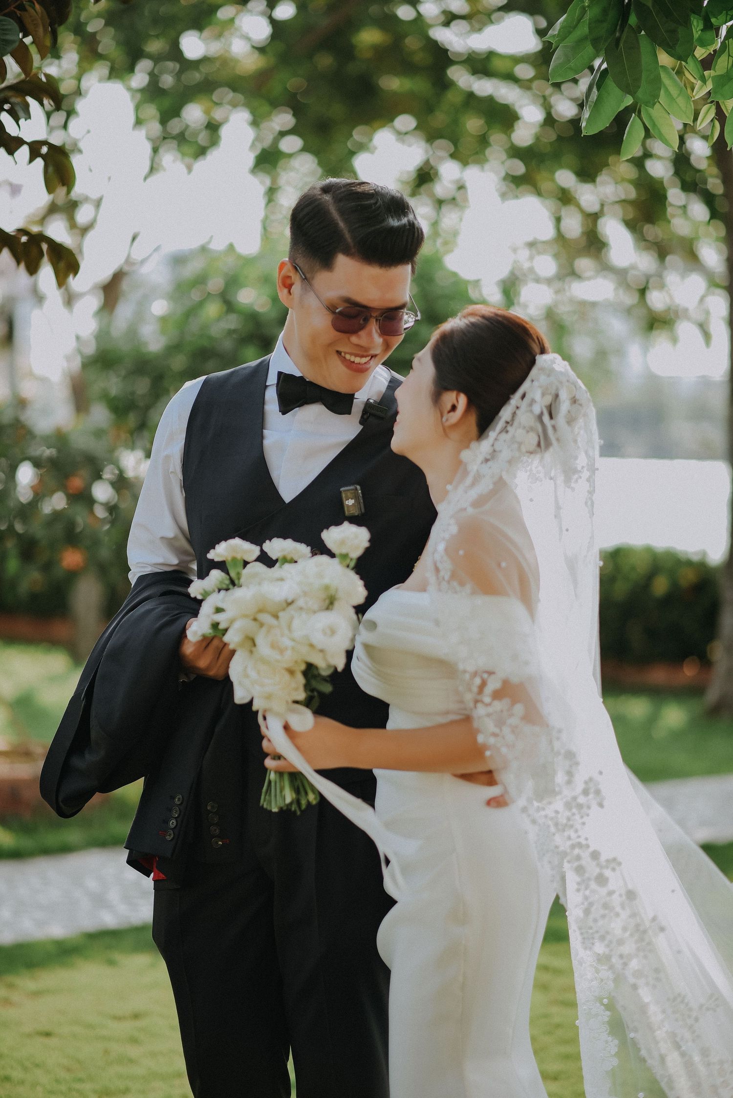 Romantic wedding couple sharing intimate moment in garden setting with white floral bouquet.