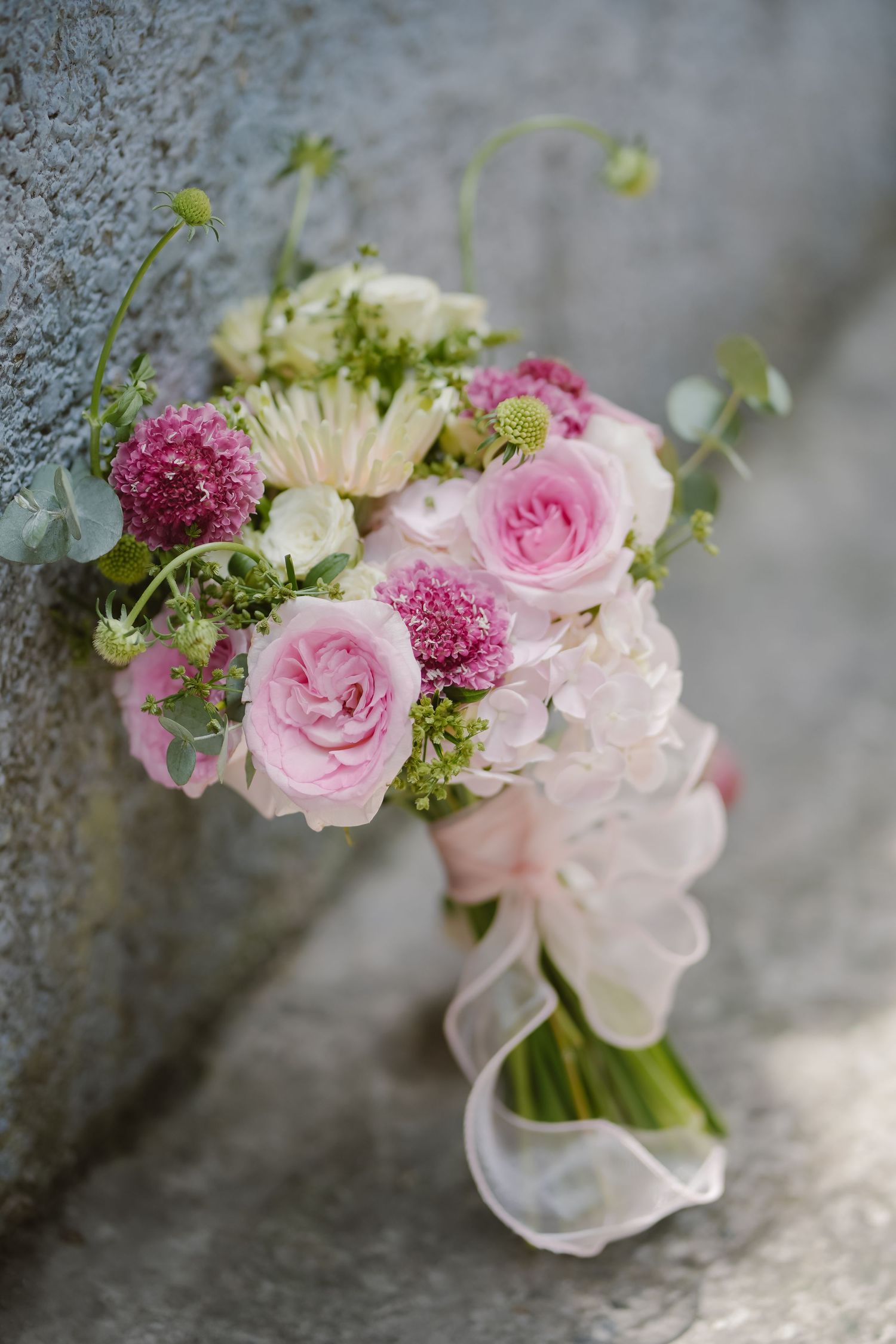 Elegant bridal bouquet with pink roses and mixed flowers wrapped in white ribbon.