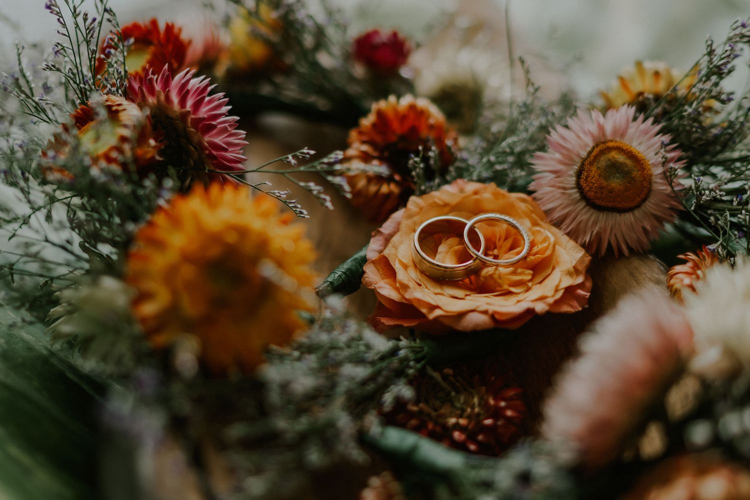 Wedding rings nestled among vibrant autumn flowers and dried botanicals in a rustic arrangement.