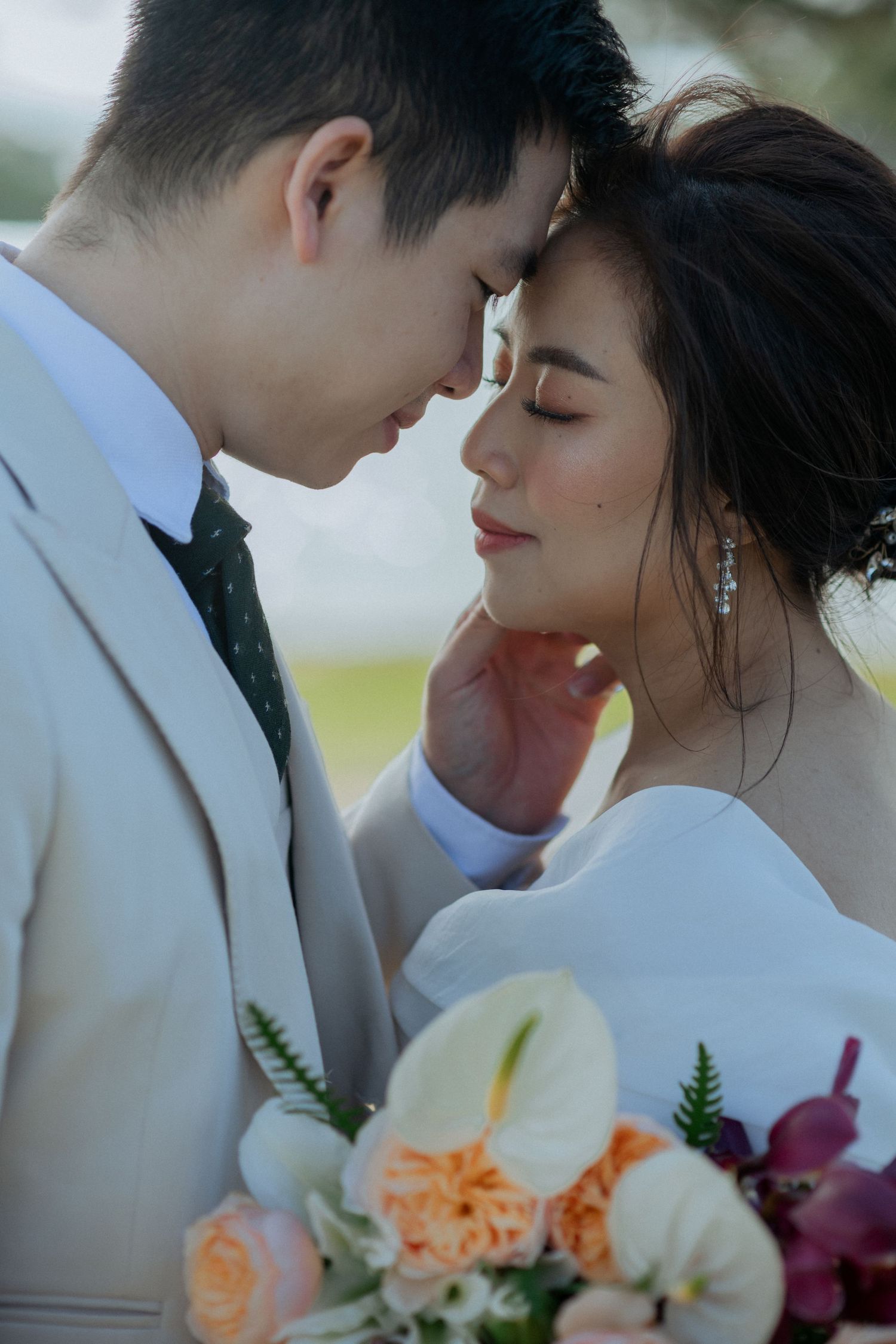 A romantic wedding couple share an intimate moment with a colorful bouquet of white lilies and peach roses.