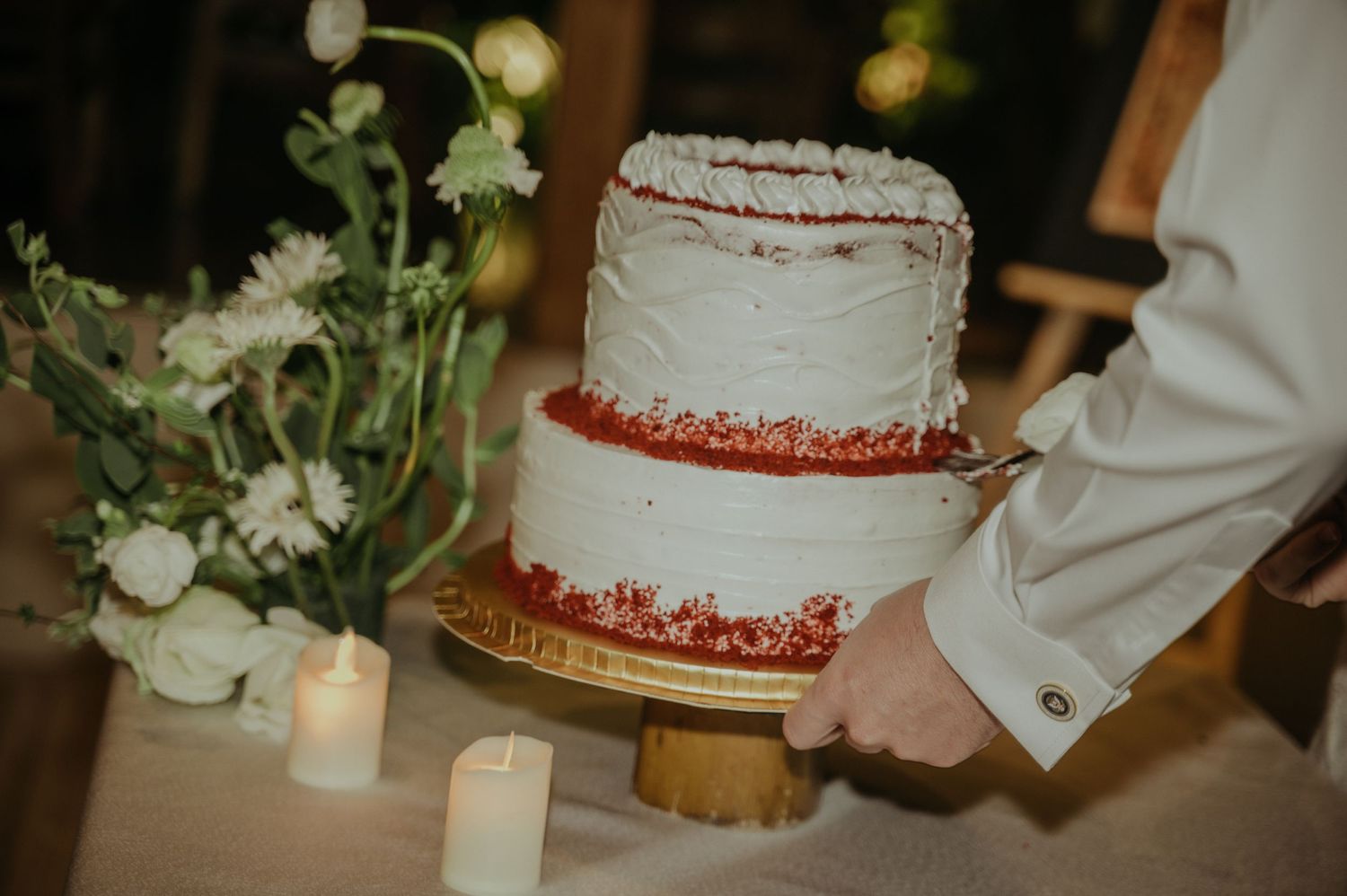 Two-tiered white wedding cake with red details and floral decorations.
