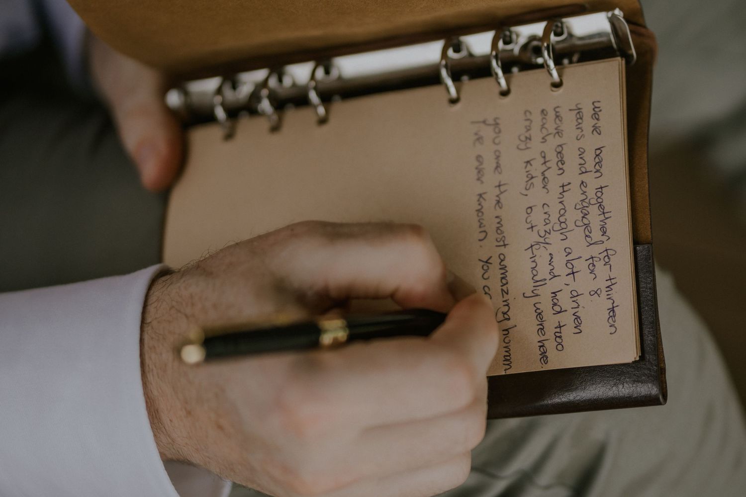 A hand writing in a spiral-bound notebook with a gold pen against a white surface.