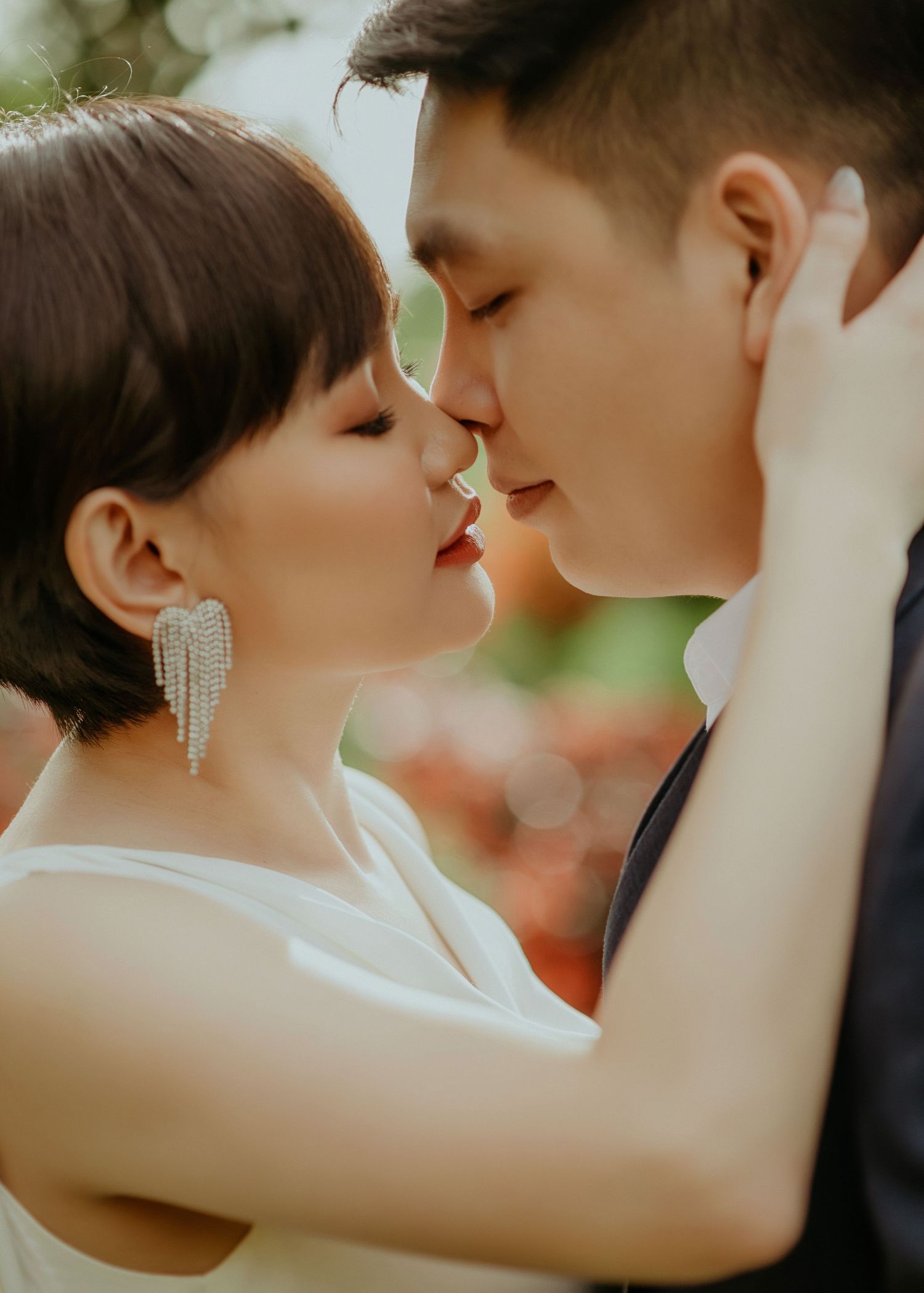 A romantic close-up portrait of a couple in wedding attire sharing an intimate moment with sunlit bokeh in the background.