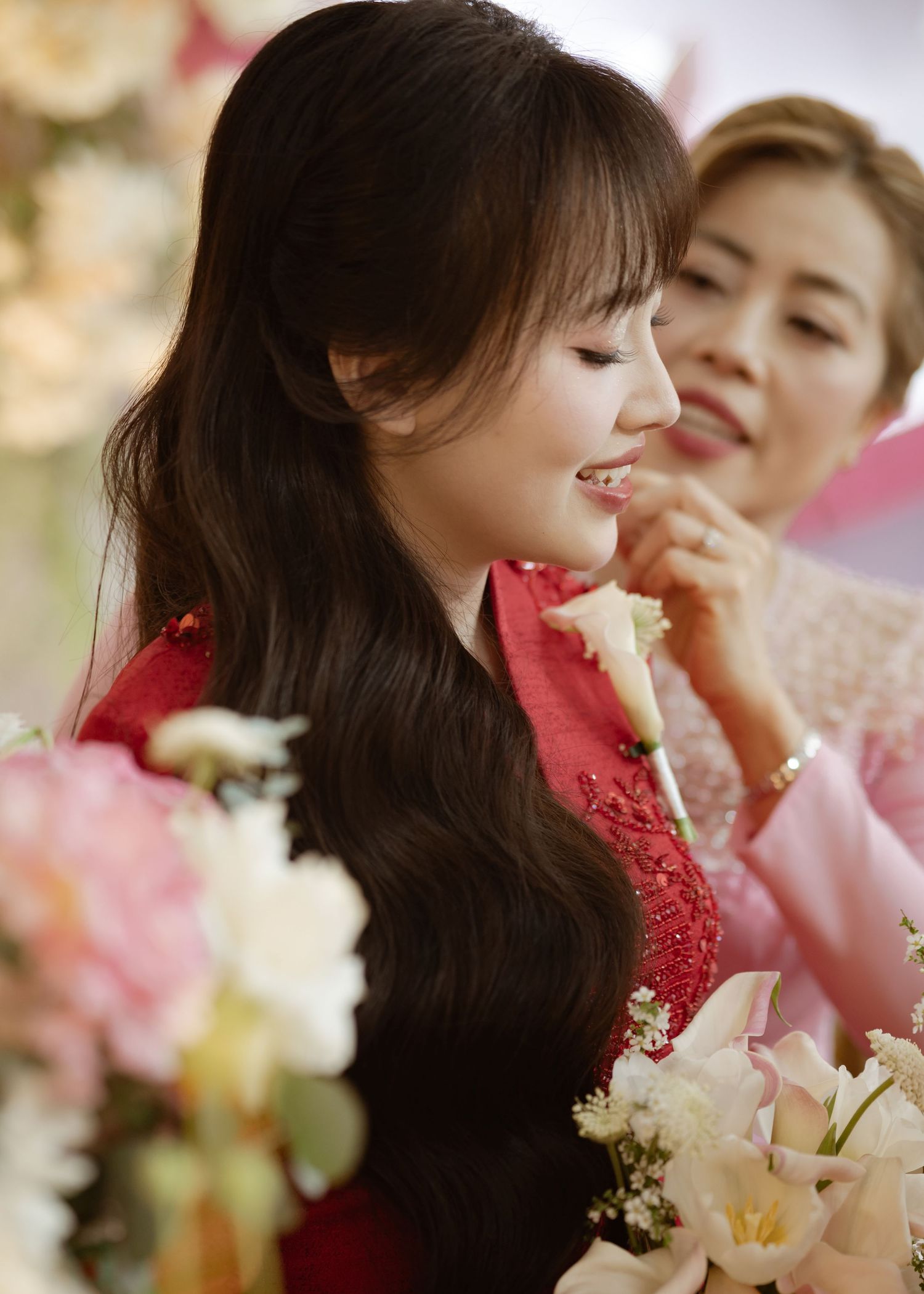 Woman in red lace dress smiling with long dark hair among pink and white flowers at elegant celebration.