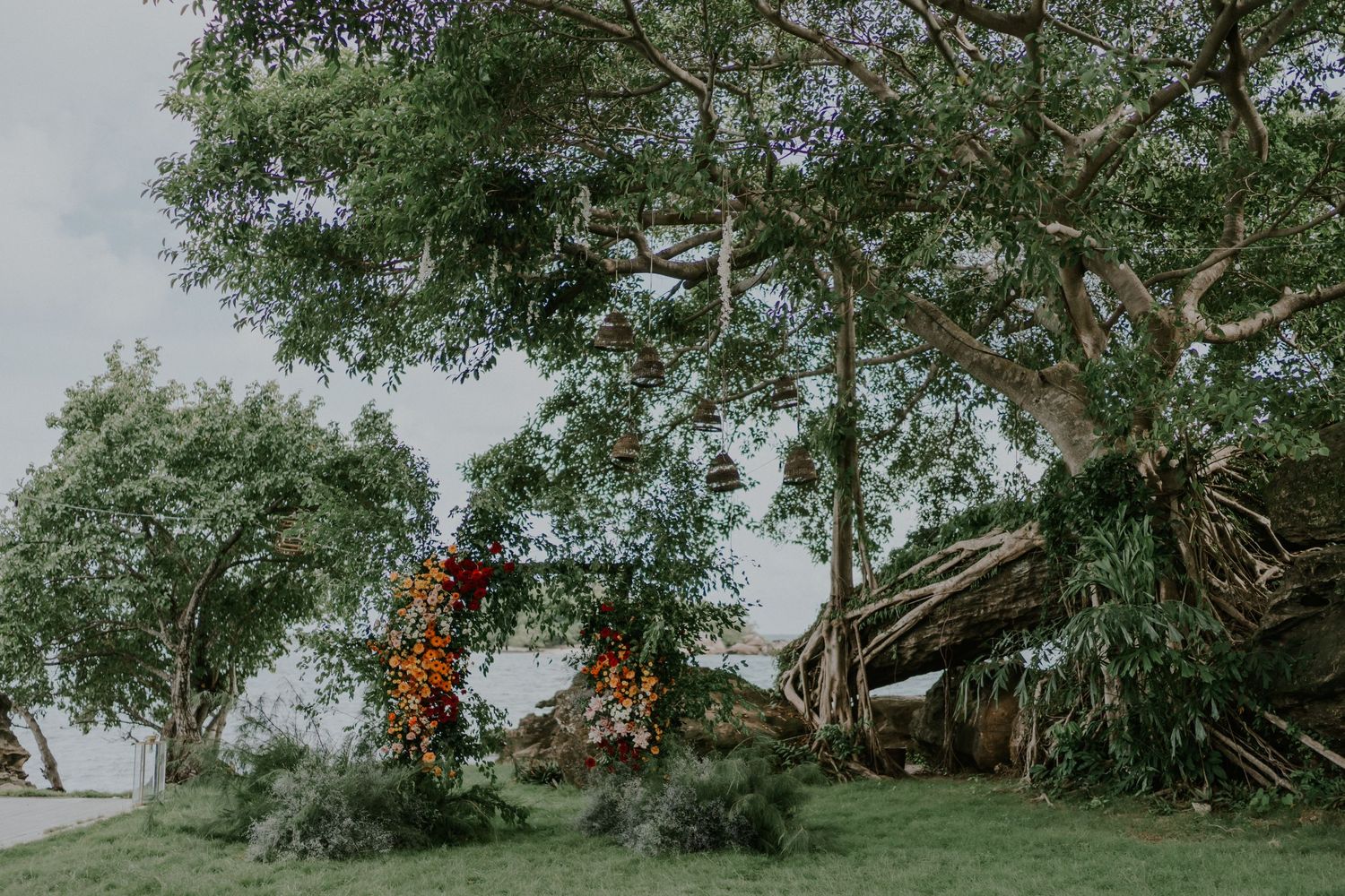 Tropical garden scene with orange floral arch beneath sprawling tree canopy.