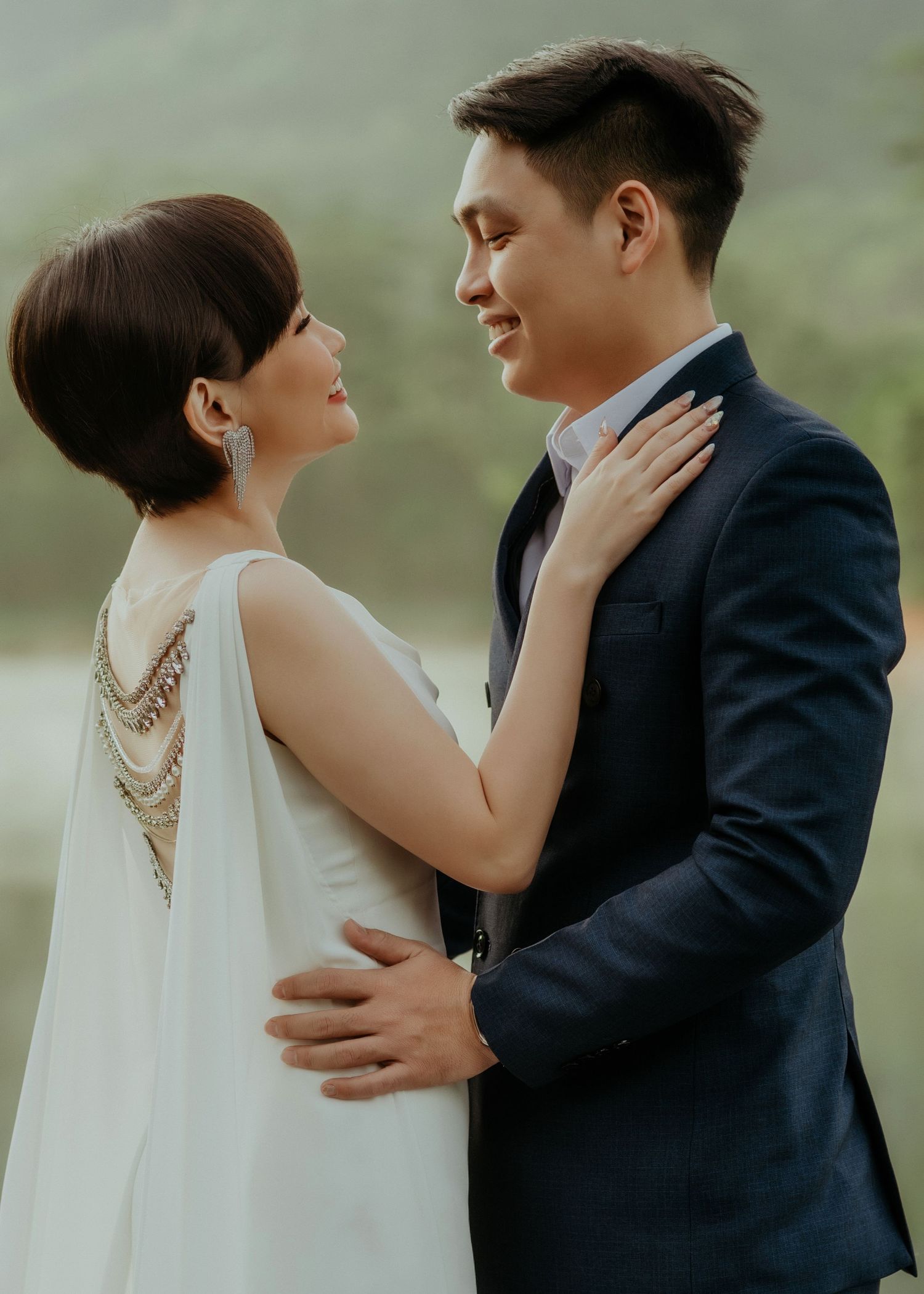 Romantic couple in formal wedding attire embracing outdoors with hazy mountains in background.