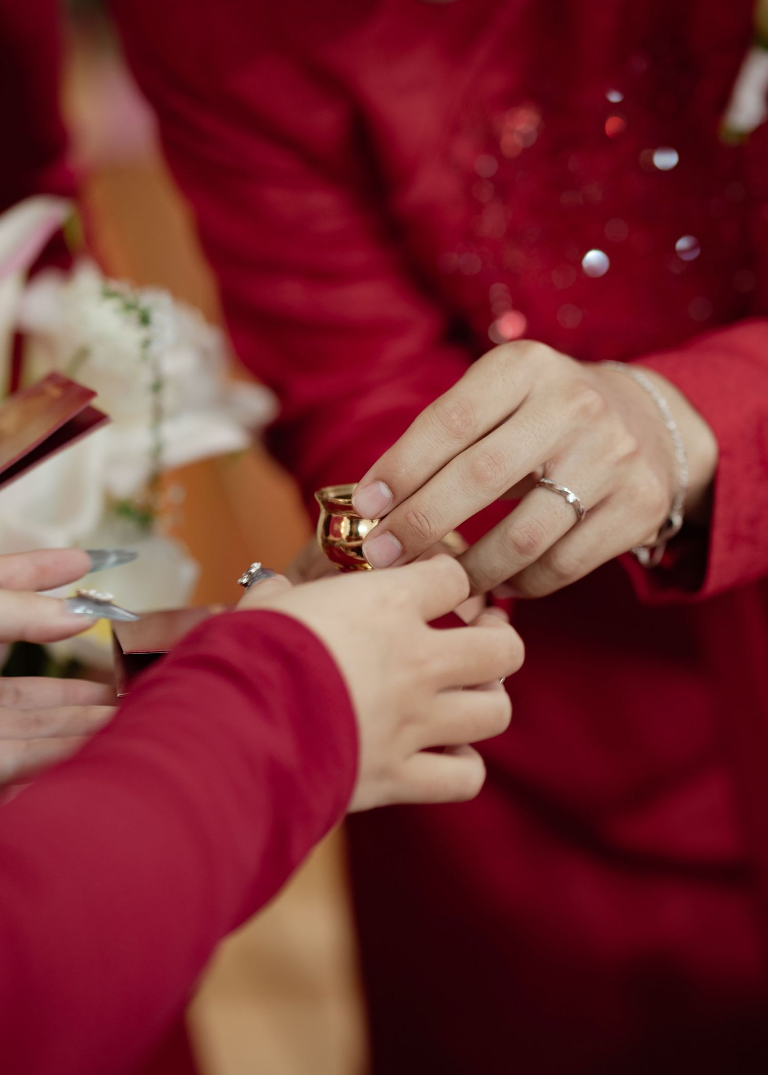 Hands wearing red sleeves exchange rings during an intimate wedding ceremony moment.