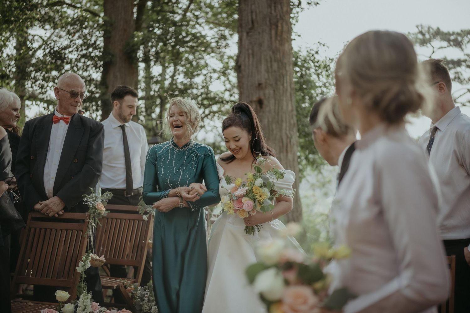 A joyful outdoor wedding ceremony in a wooded setting with natural decor and floral bouquets.