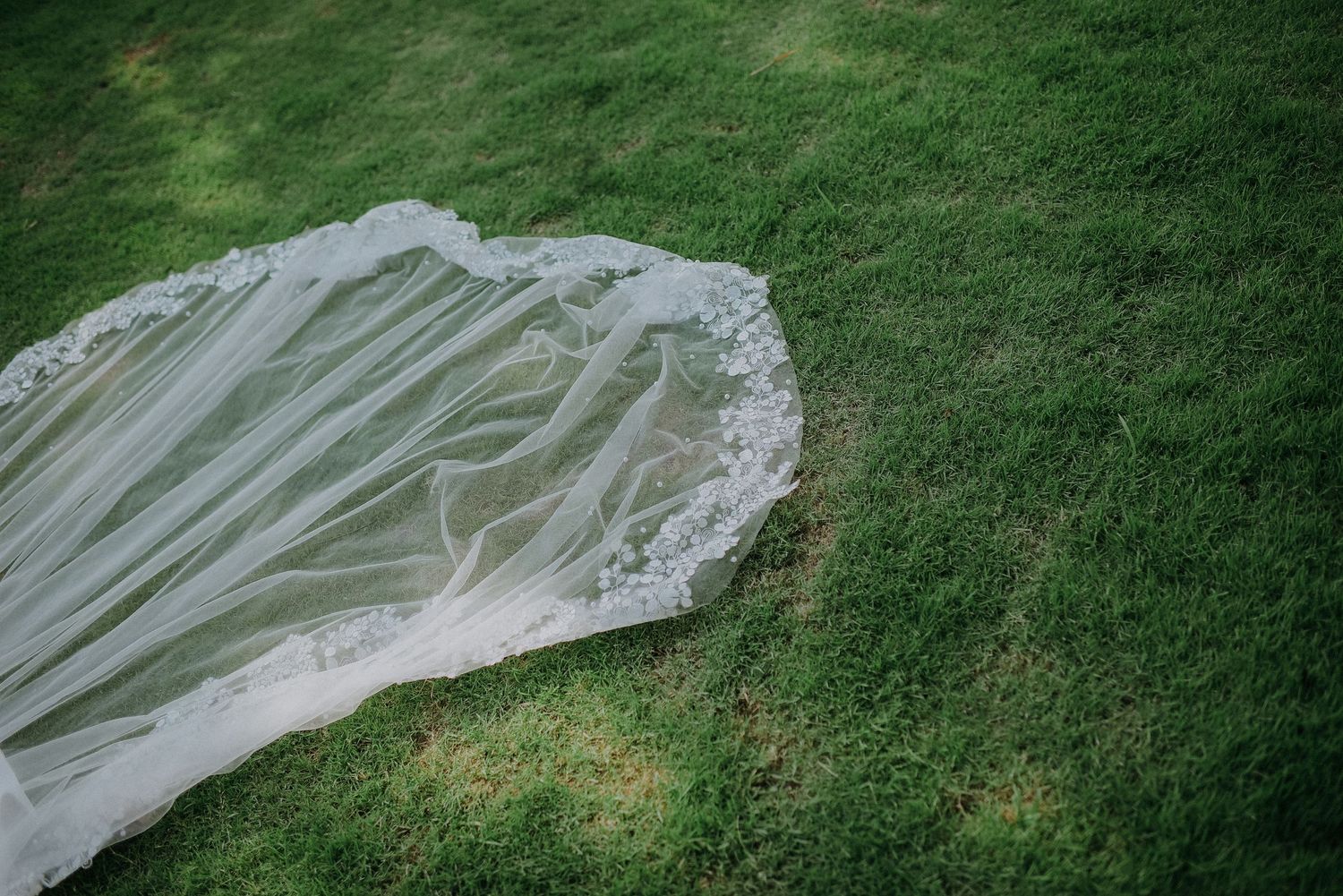 Delicate lace-trimmed wedding veil laid out on green grass showing intricate details.