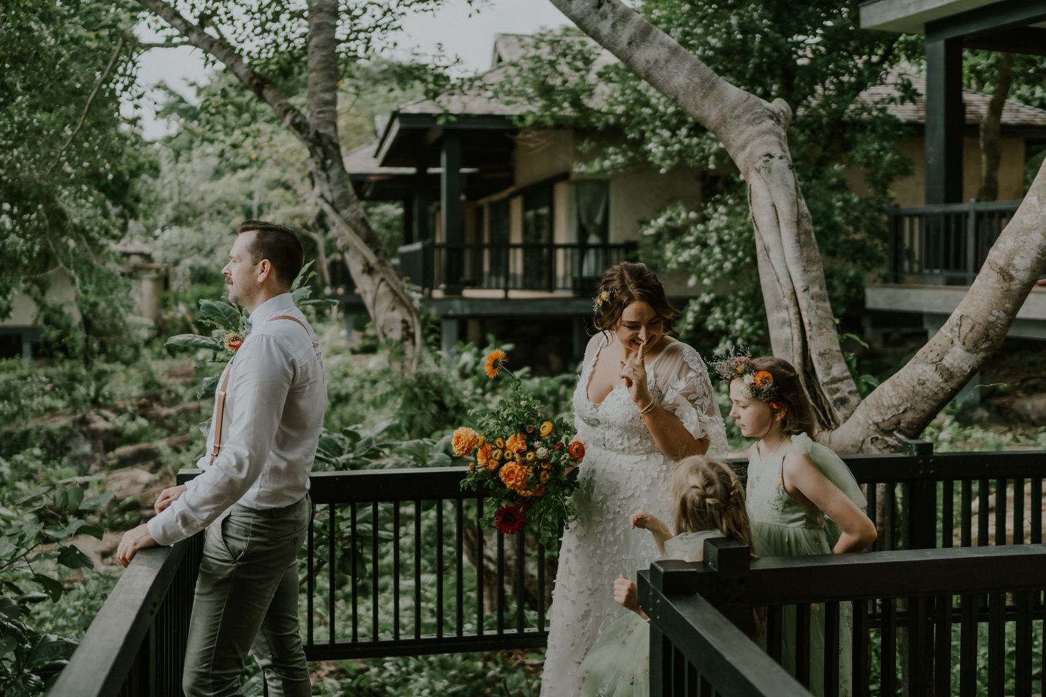 A candid wedding moment captured on a wooden deck with greenery and orange floral arrangements.