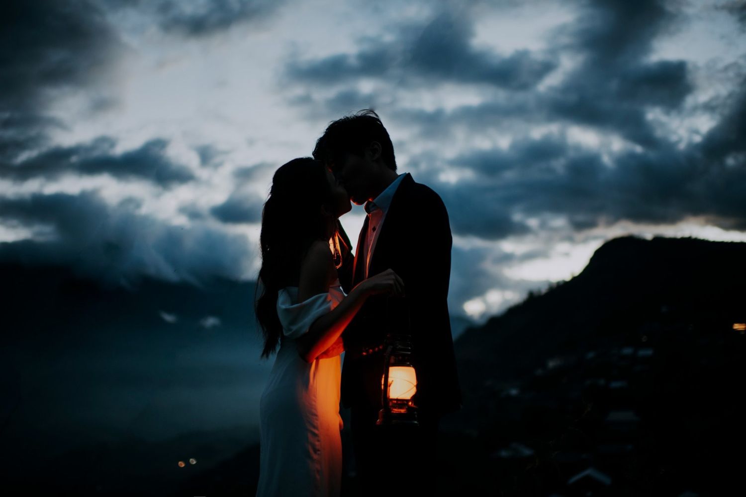 A romantic silhouette of a couple embracing at dusk with a lantern creating warm backlight.