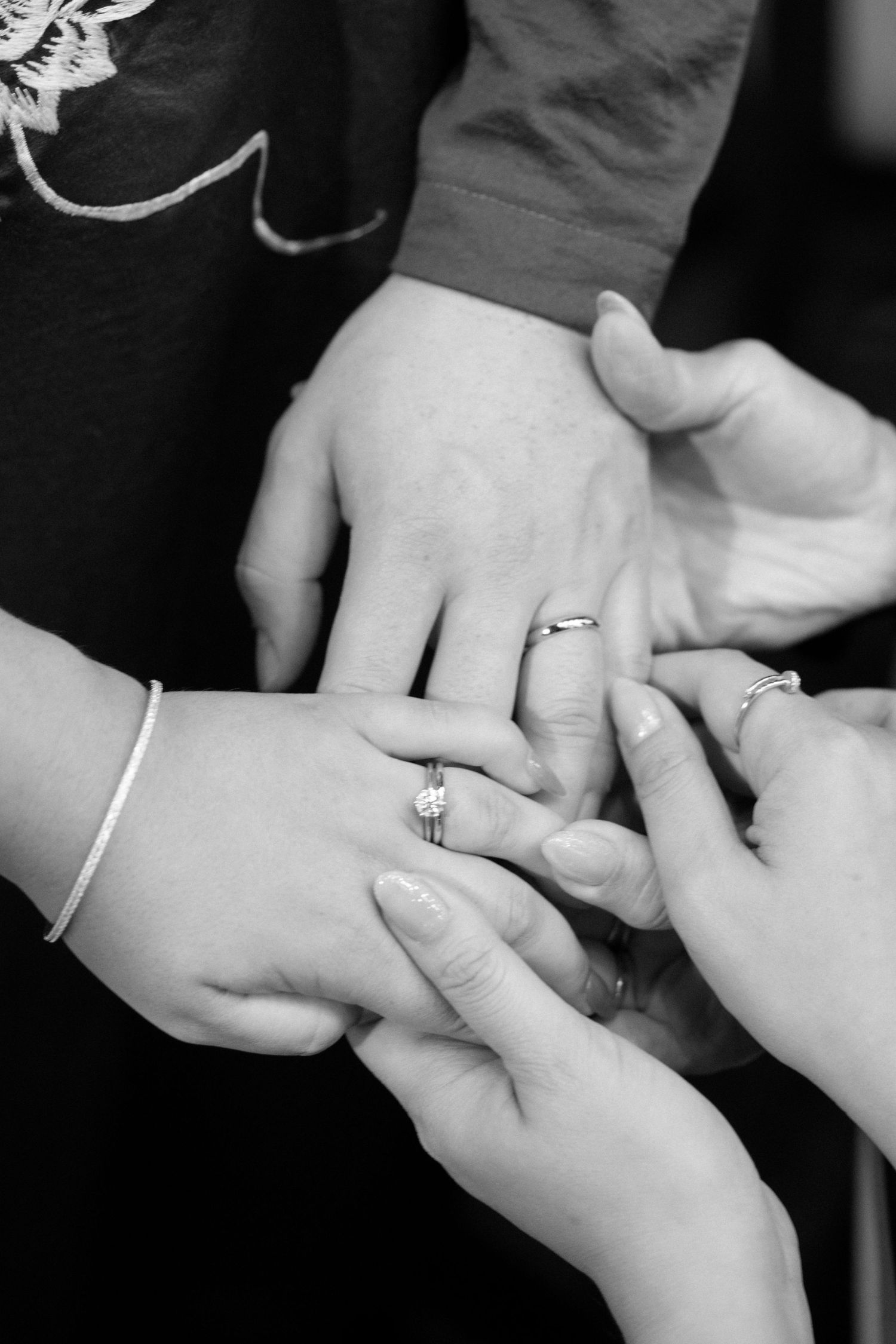 Black and white close-up of hands admiring engagement rings and wedding bands.