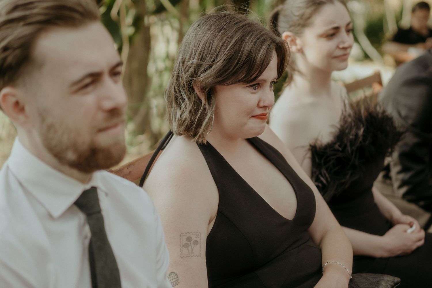 A group of guests in formal attire stand together at an outdoor social gathering.