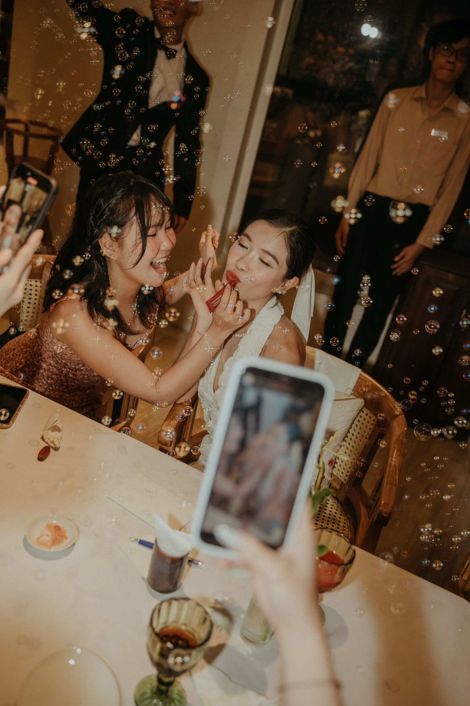 Friends celebrating at a dinner party with smartphones capturing candid moments under warm lighting.