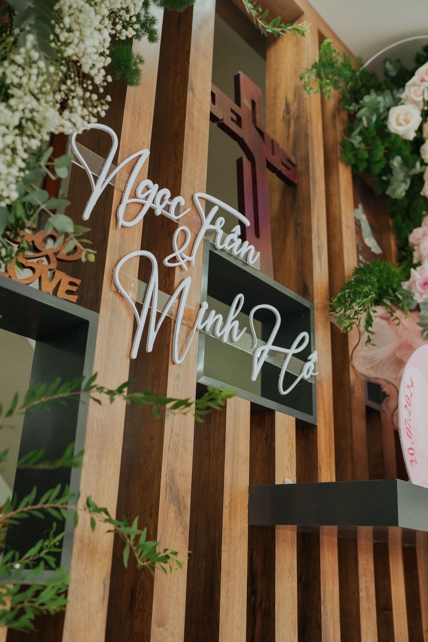 Wooden slat wall with decorative white text signage surrounded by floral arrangements.