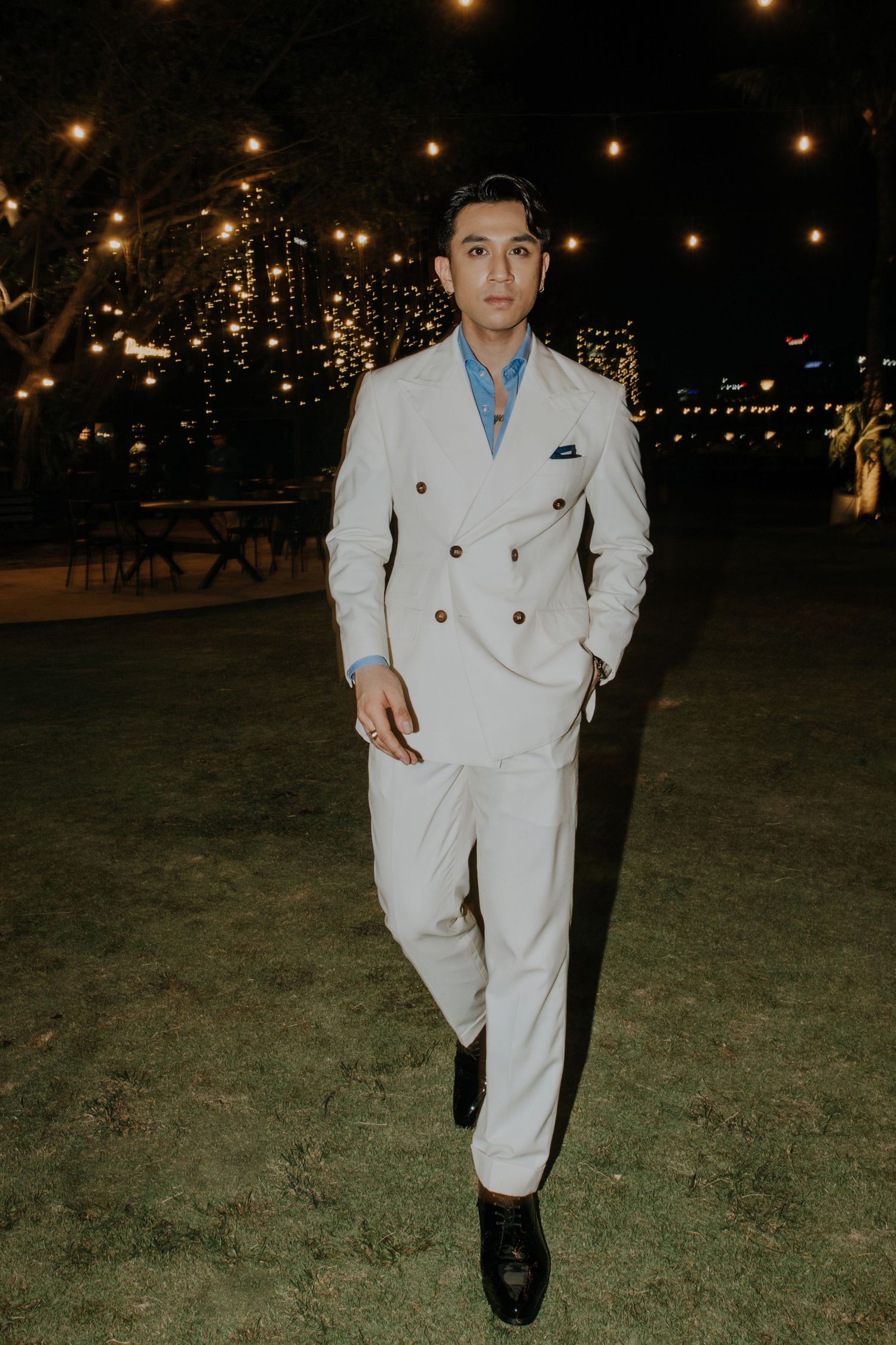 An elegant nighttime portrait of someone wearing a white double-breasted suit with a blue shirt.