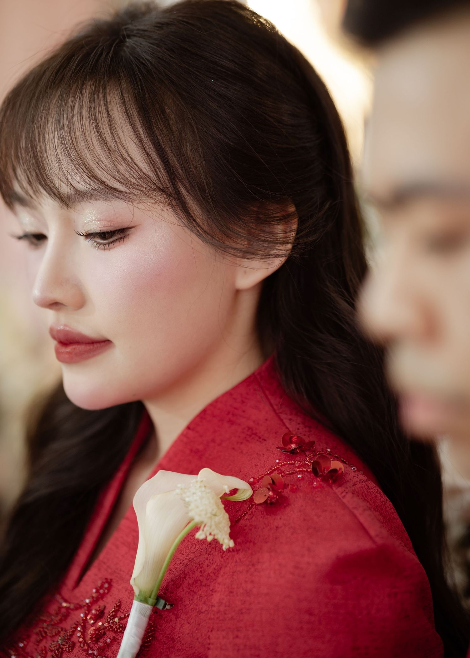 Profile view of someone wearing a traditional red qipao dress with a white calla lily corsage and natural makeup look.