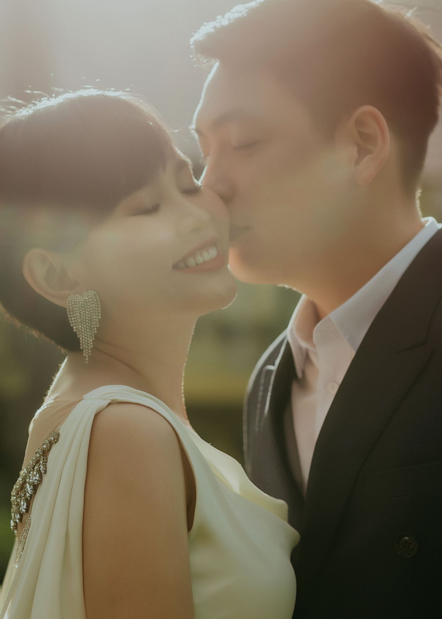 A couple enjoying an intimate romantic moment in warm sunlight wearing elegant wedding attire.