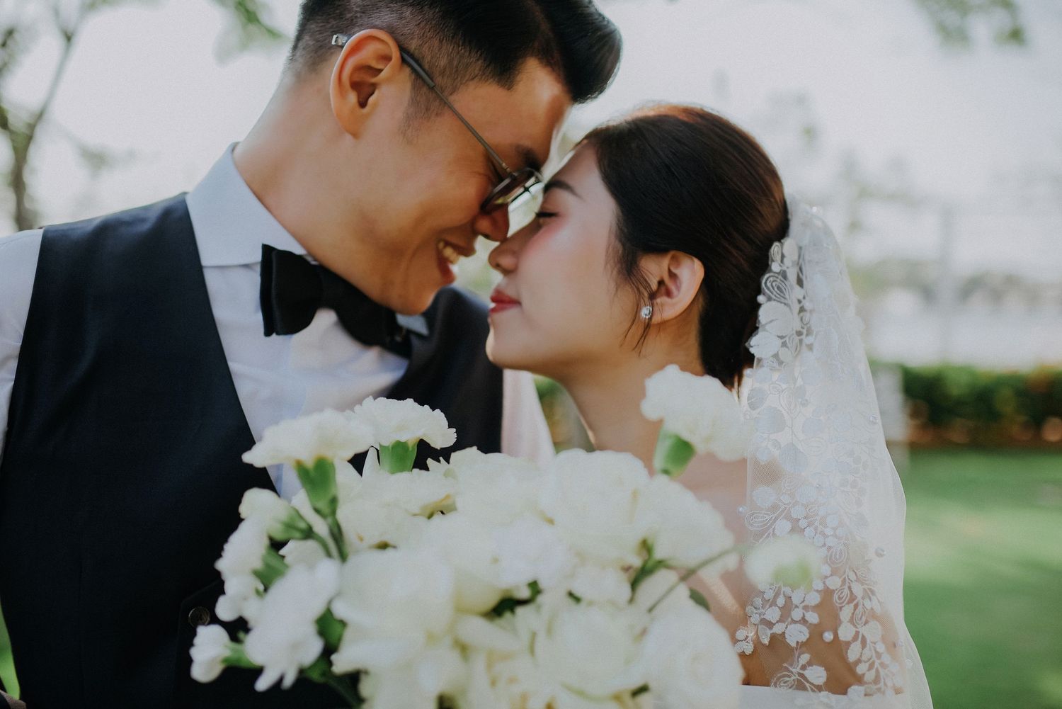 Romantic wedding portrait set against a lush garden backdrop with white floral bouquet.