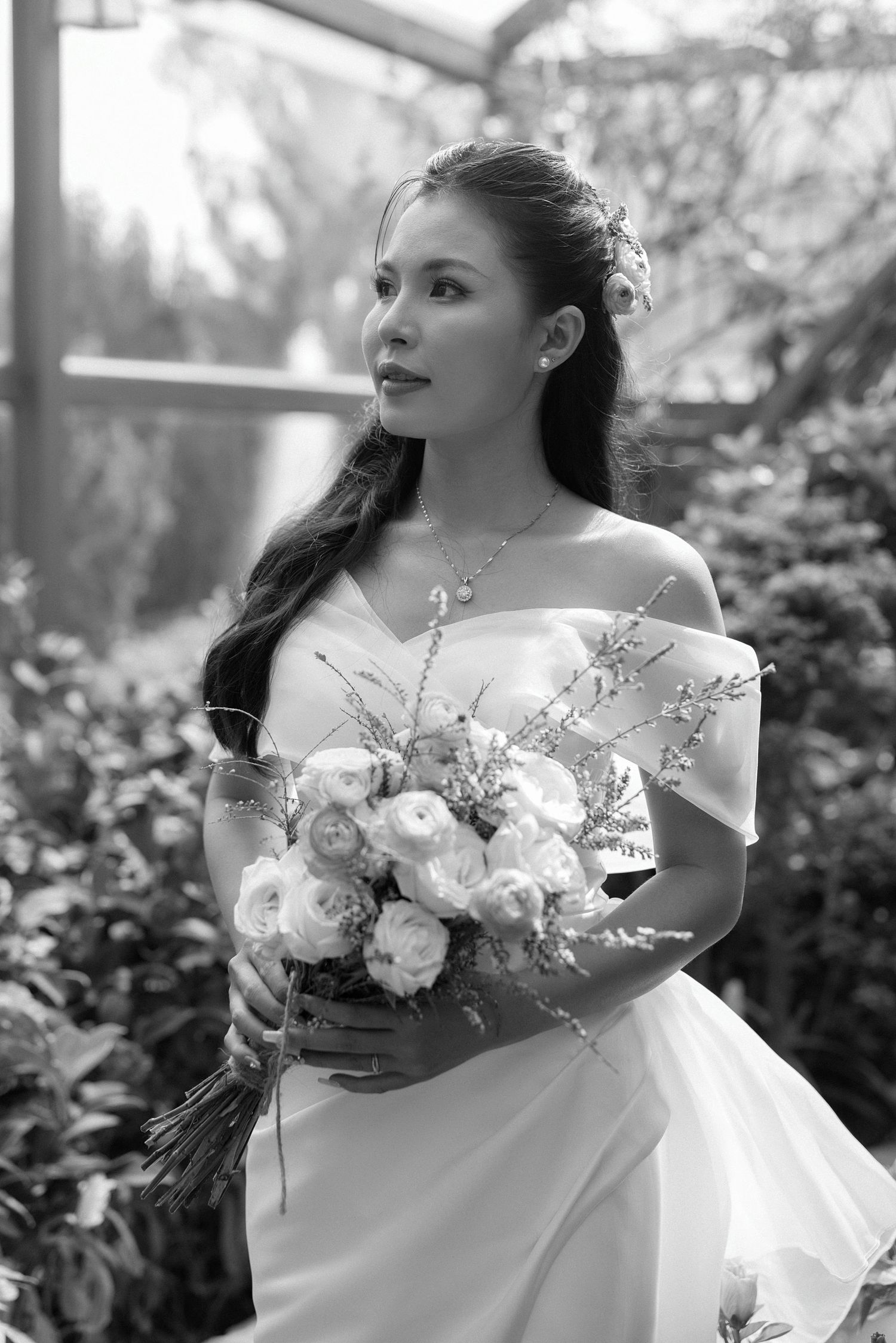 Black and white portrait of a bride in an off-shoulder wedding dress holding an elegant bouquet of roses and flowers.