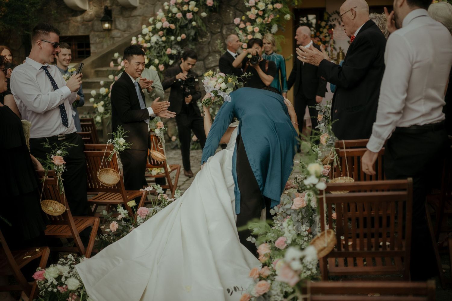 Wedding ceremony at a rustic venue decorated with lush floral arrangements and wooden chairs.