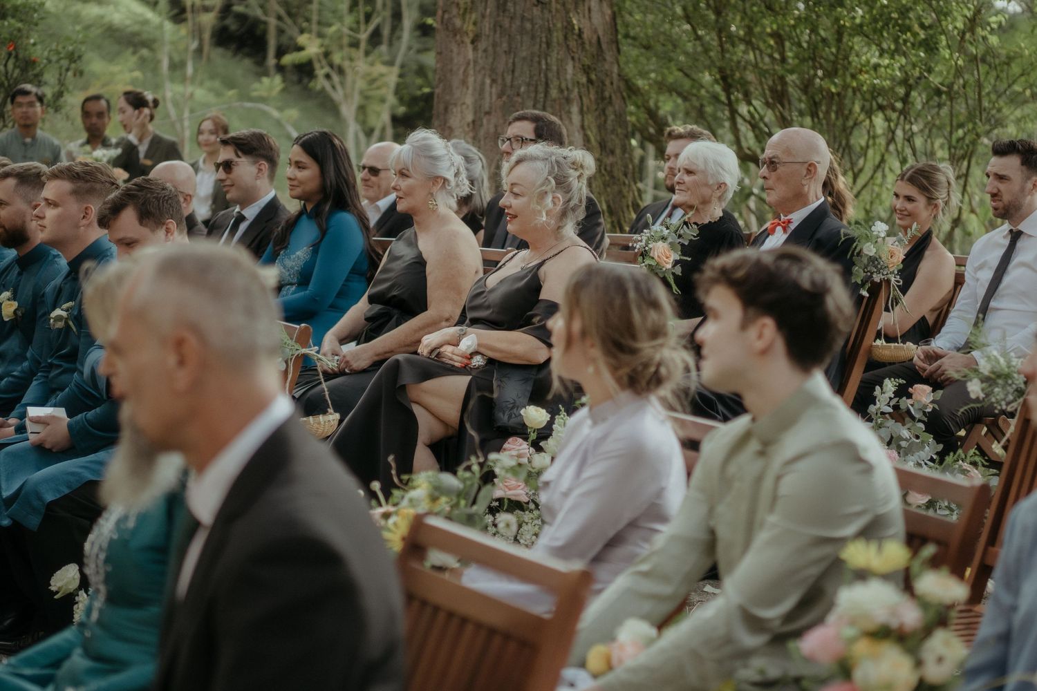 Guests seated on wooden chairs during an outdoor wedding ceremony in a lush garden setting.