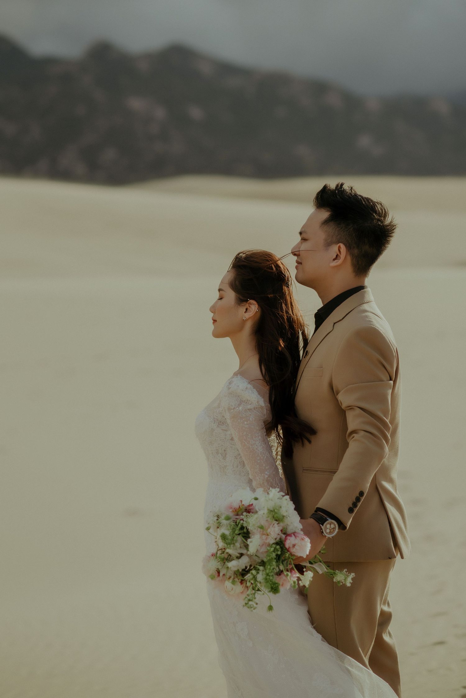 A couple in wedding attire poses intimately in a desert setting with soft lighting and a romantic atmosphere.