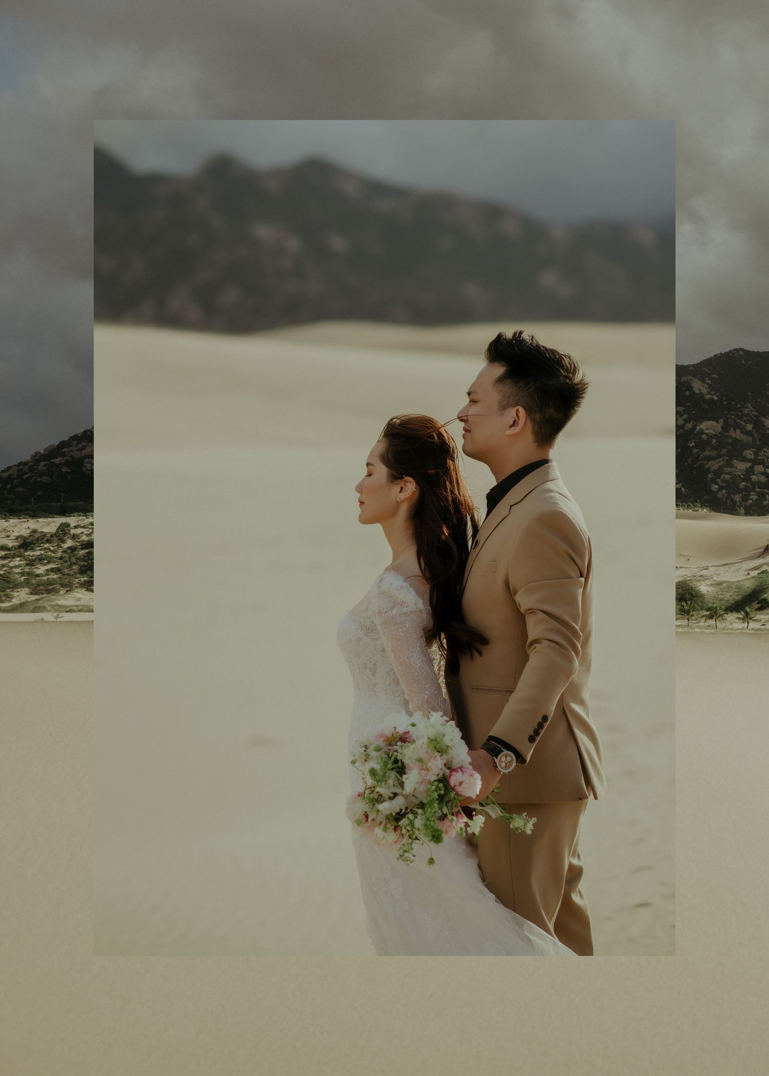 A couple in wedding attire poses together against a scenic desert landscape with mountains in the background.