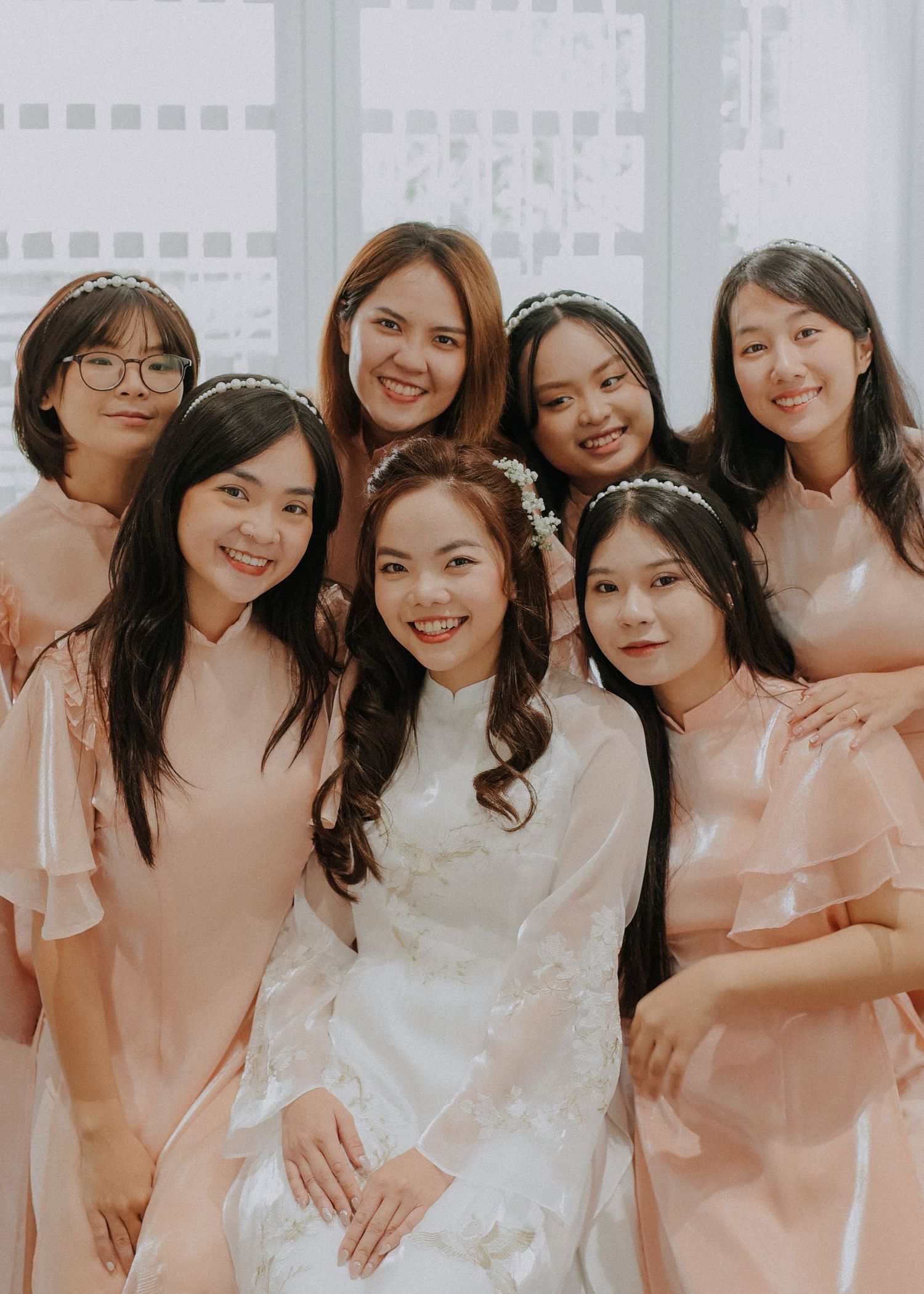 Wedding party portrait with bridesmaids in peach dresses surrounding bride in white traditional dress.