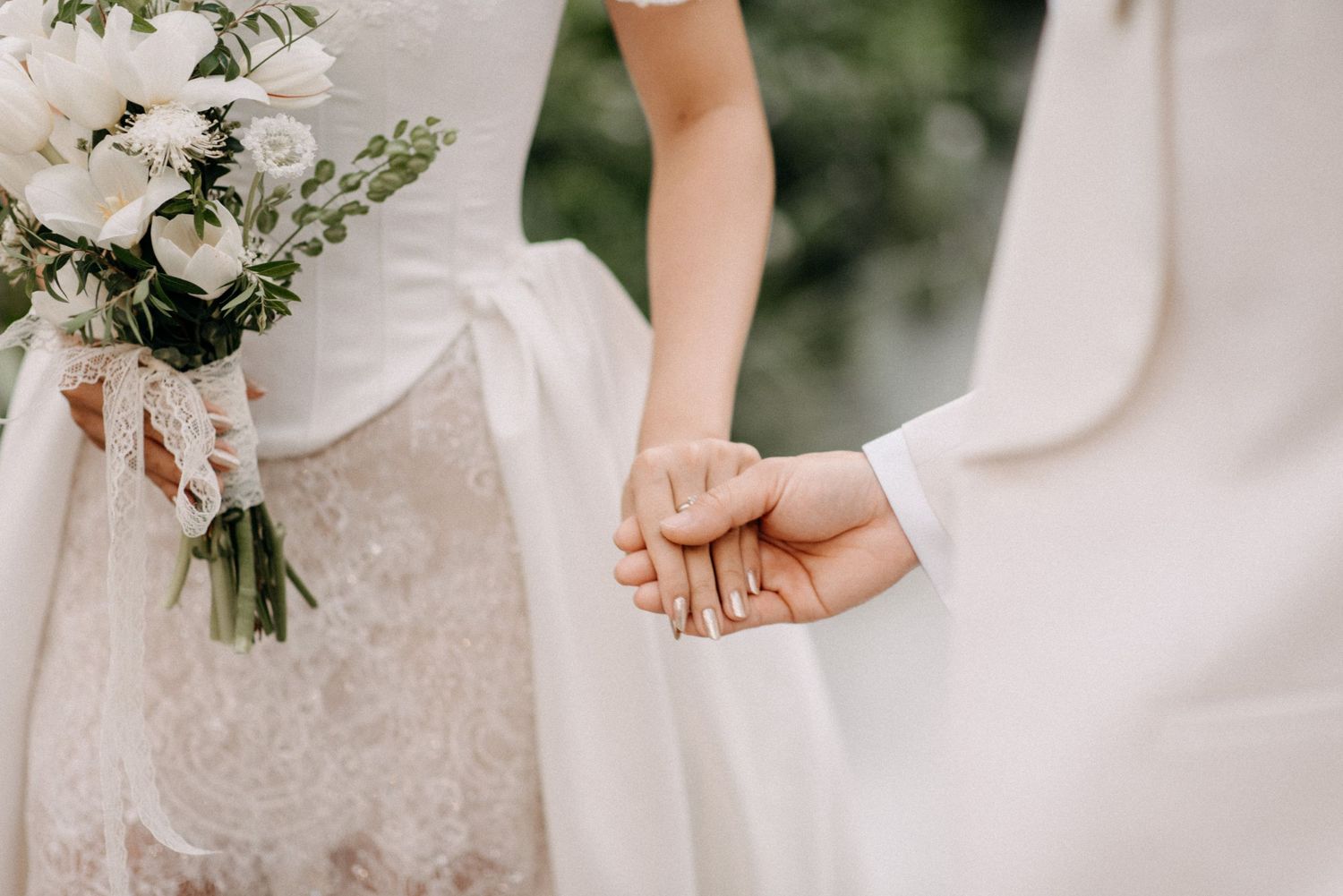 Close-up of newlyweds holding hands, showing lace dress details and white bouquet.
