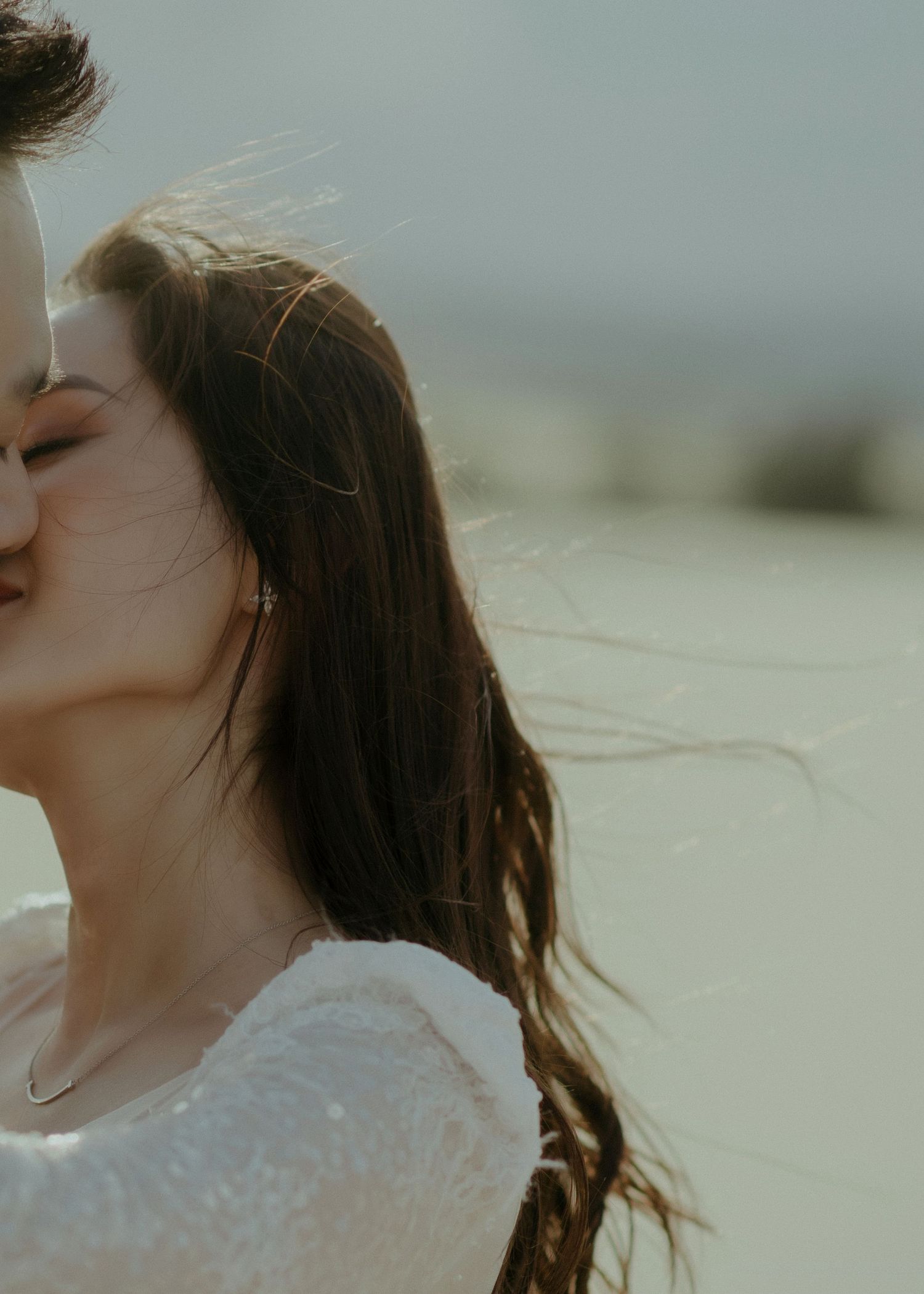 A romantic moment captured with wind-blown hair and soft lighting as a couple shares an intimate embrace.