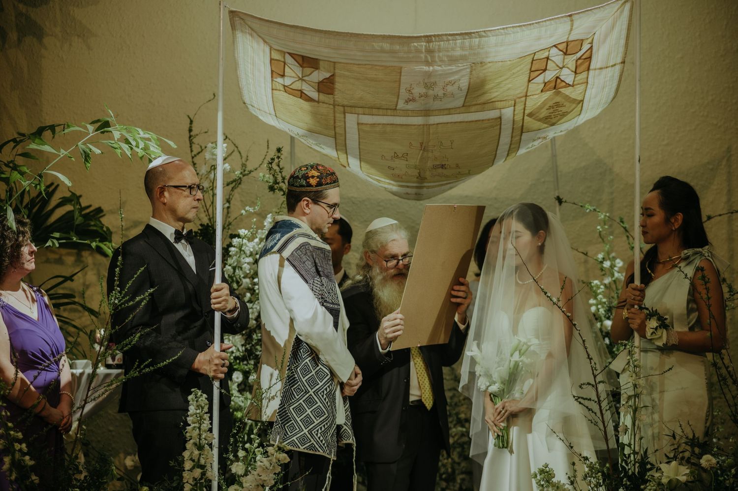 A traditional Jewish wedding ceremony with a chuppah decorated with flowers and greenery.