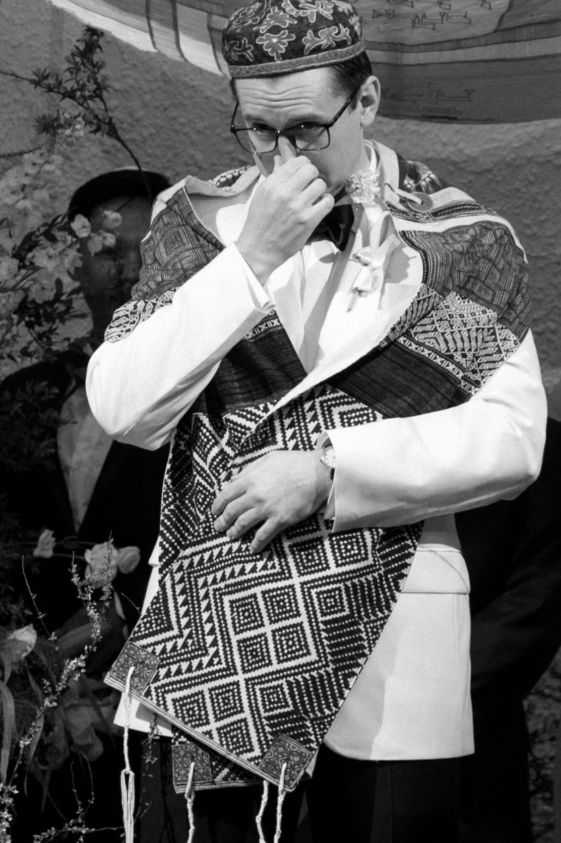 Black and white photo of someone in traditional ceremonial attire wiping their eyes during an emotional moment.