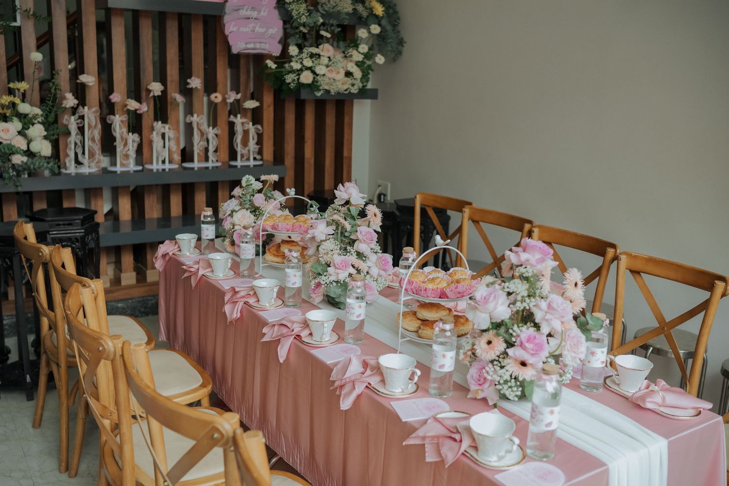 Elegantly decorated tea ceremony table with pink tablecloth and cross-back chairs.