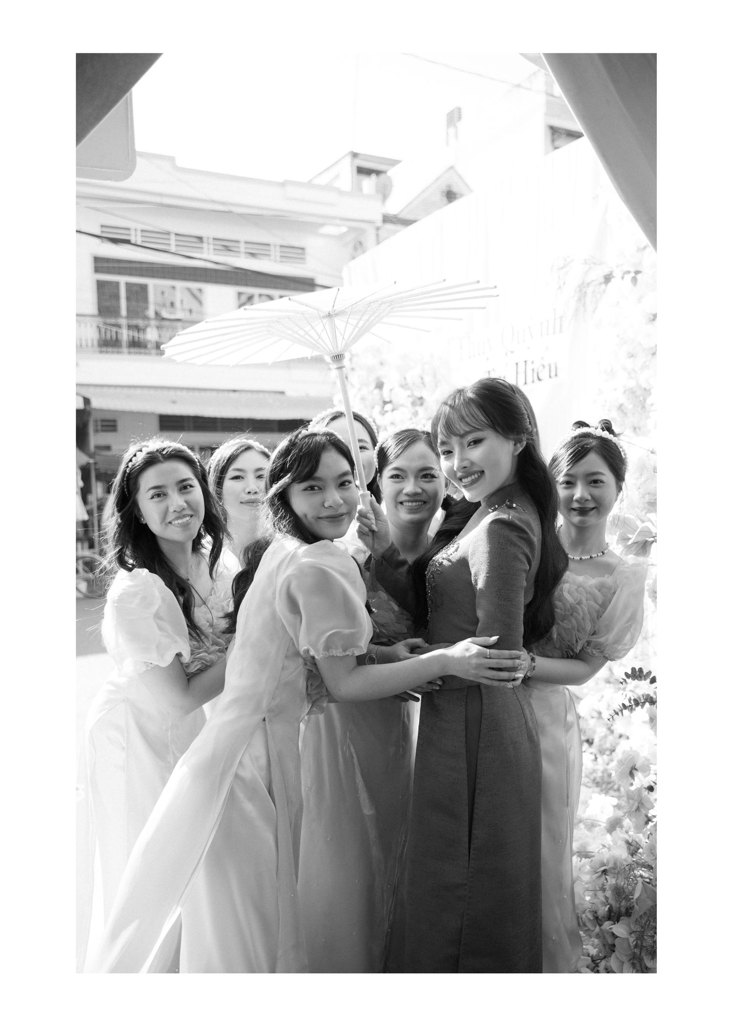 A group of bridesmaids in light-colored dresses share a joyful moment together at an outdoor wedding venue.