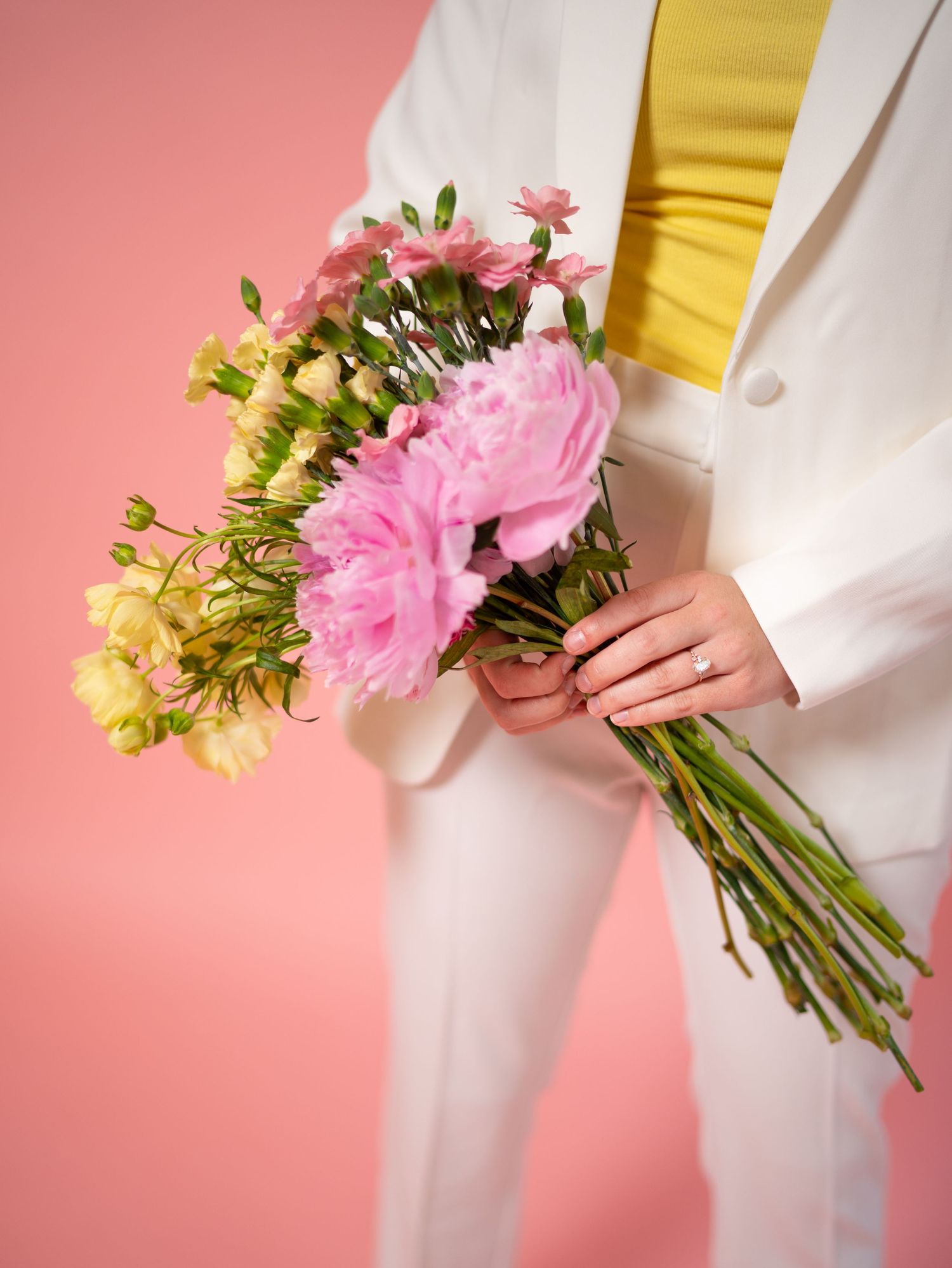 Close-up of person in white suit and yellow top holding fresh floral arrangement.