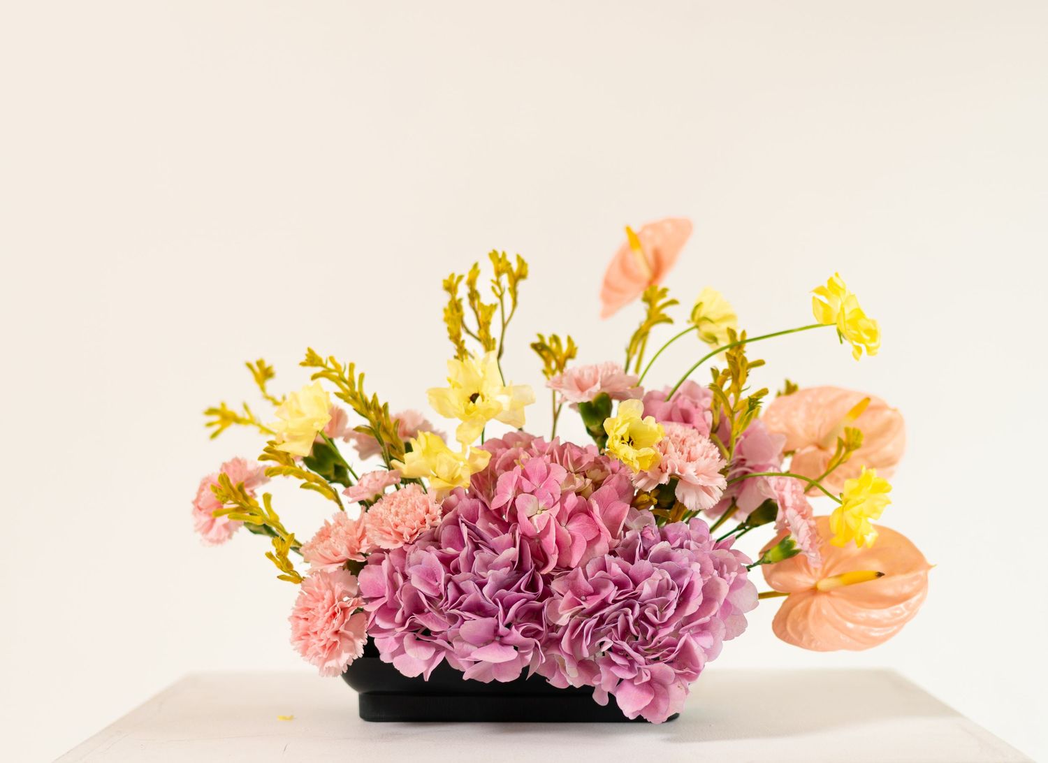 Multiple vases filled with pastel pink and yellow flowers arranged in a row on a white surface against a light background.